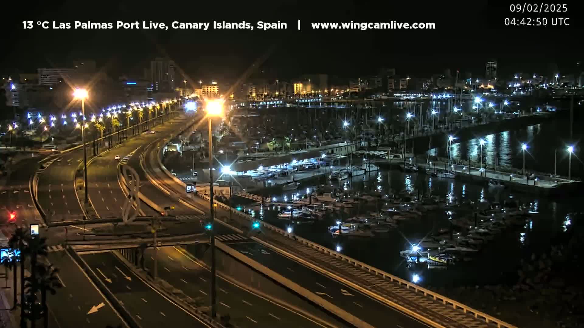 A nighttime view of a harbor filled with boats and a multi-lane highway with sparse traffic, under clear skies.