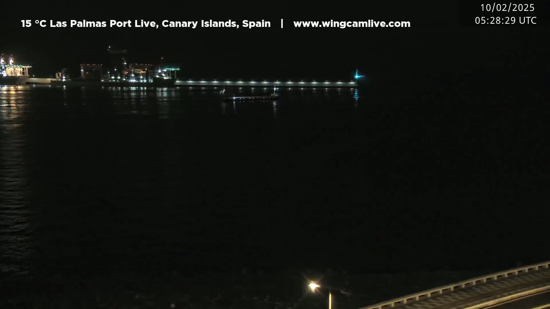 A nighttime view of a brightly lit port with several ships, a long pier, and calm water.