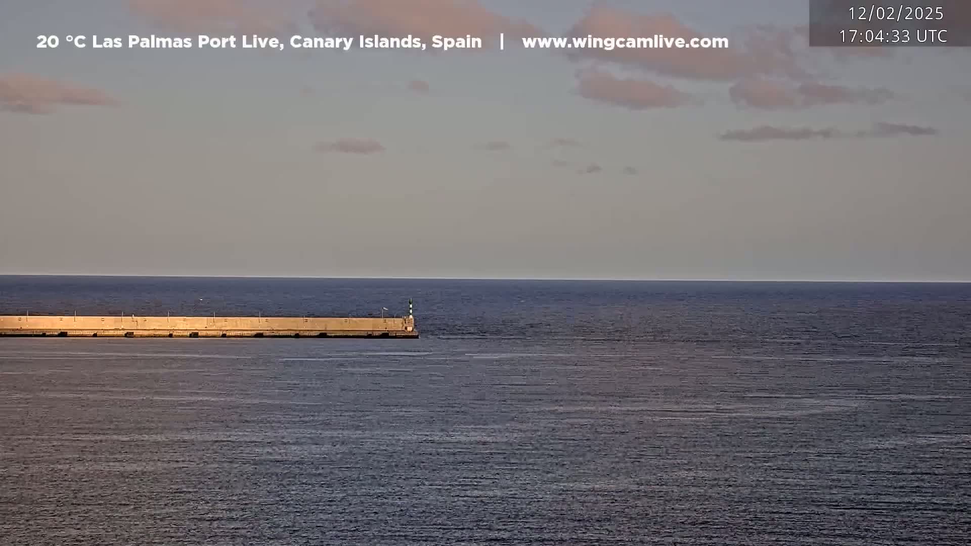 A long, low breakwater extends into a calm, dark blue ocean under a pale, mostly clear sky.