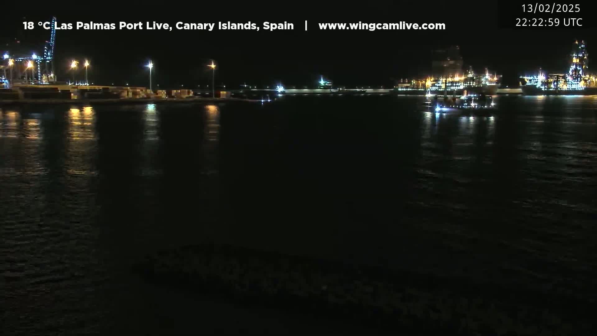 A nighttime view of a harbor with several illuminated ships and a calm, dark body of water reflecting the lights.