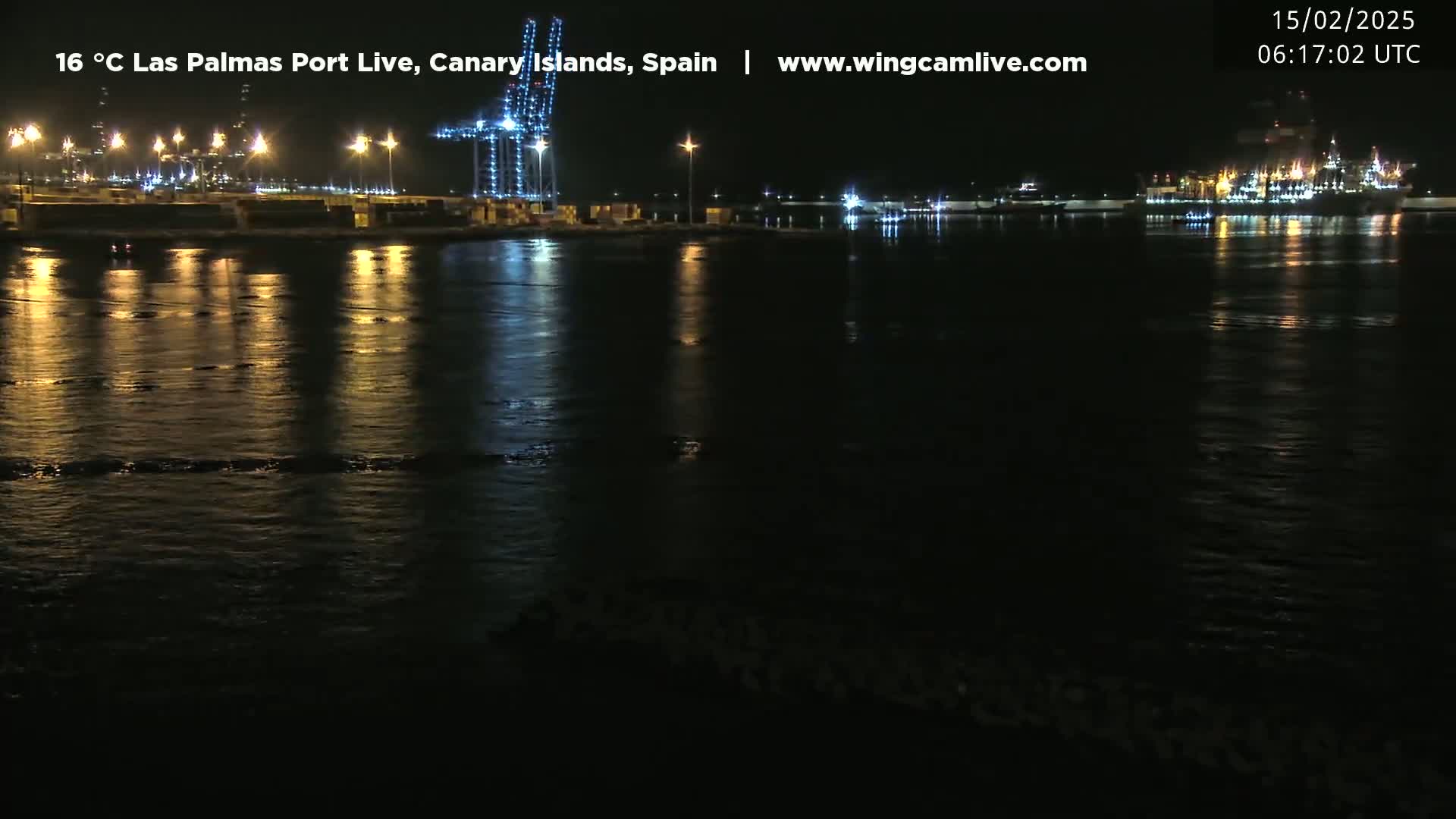 A nighttime view of a calm harbor with lights reflecting on the water, showing a port with industrial structures and cranes.