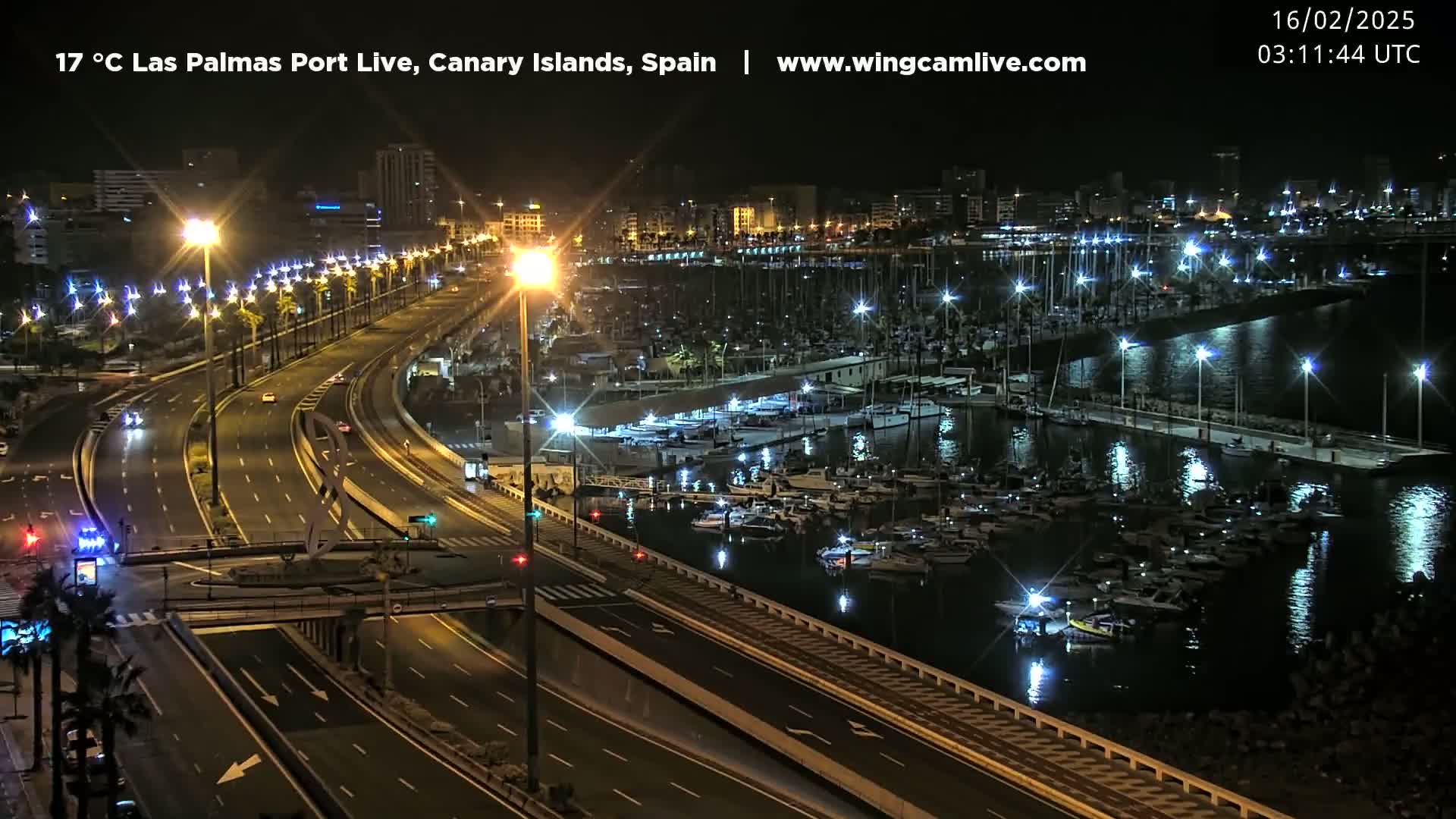 A nighttime view of a harbor filled with boats, alongside a multi-lane highway illuminated by streetlights.