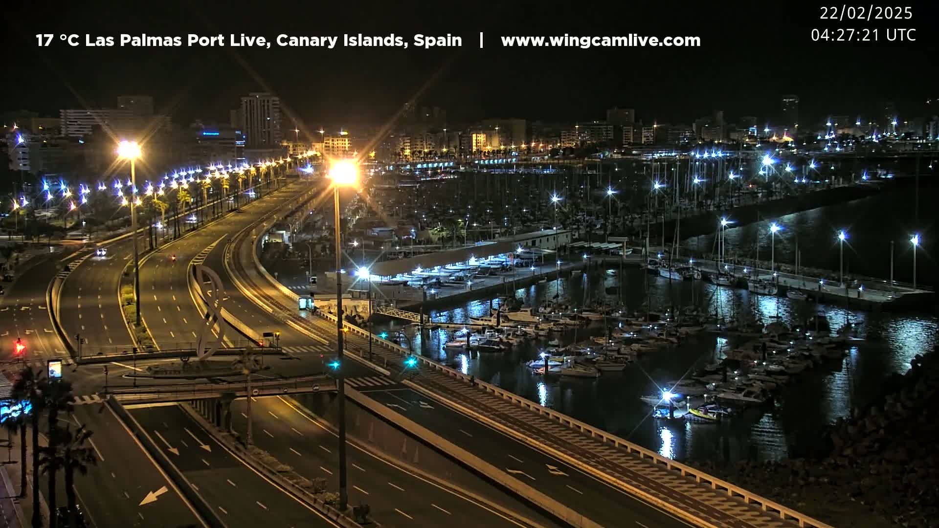 A nighttime view of a marina filled with boats, next to a multi-lane highway illuminated by streetlights.