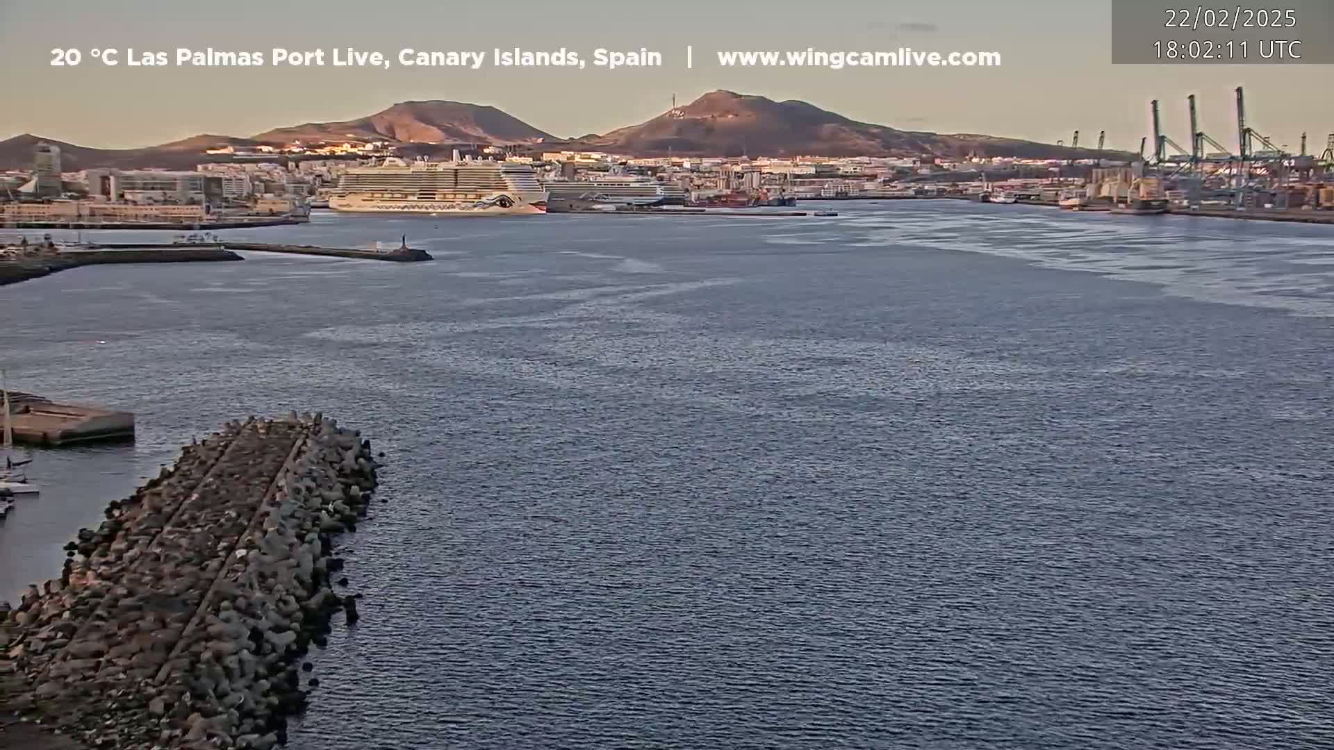 A cruise ship is docked in a calm harbor next to a city and mountains under a clear, twilight sky.