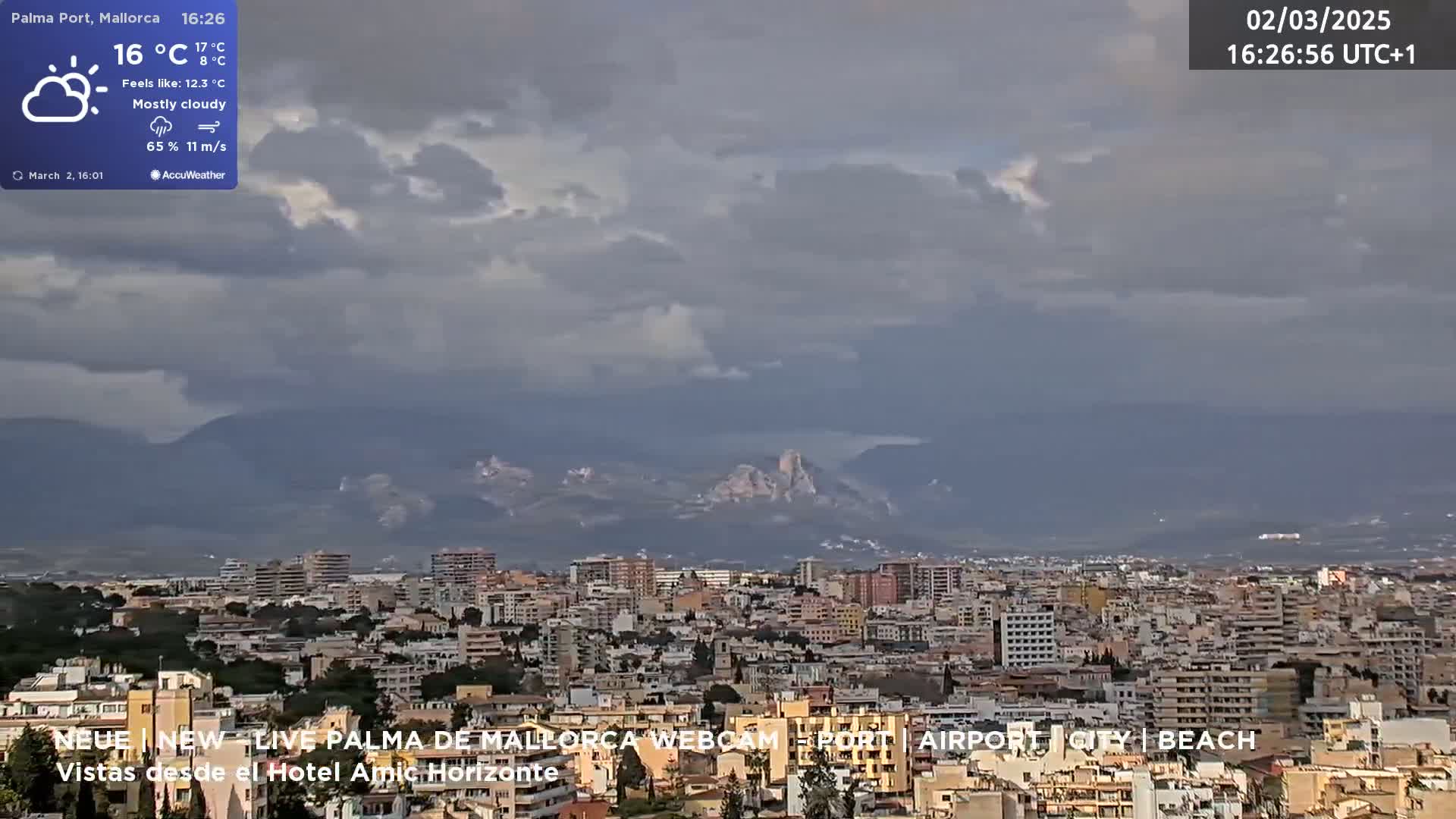 A mostly cloudy, windy cityscape with distant mountains under a gray sky.