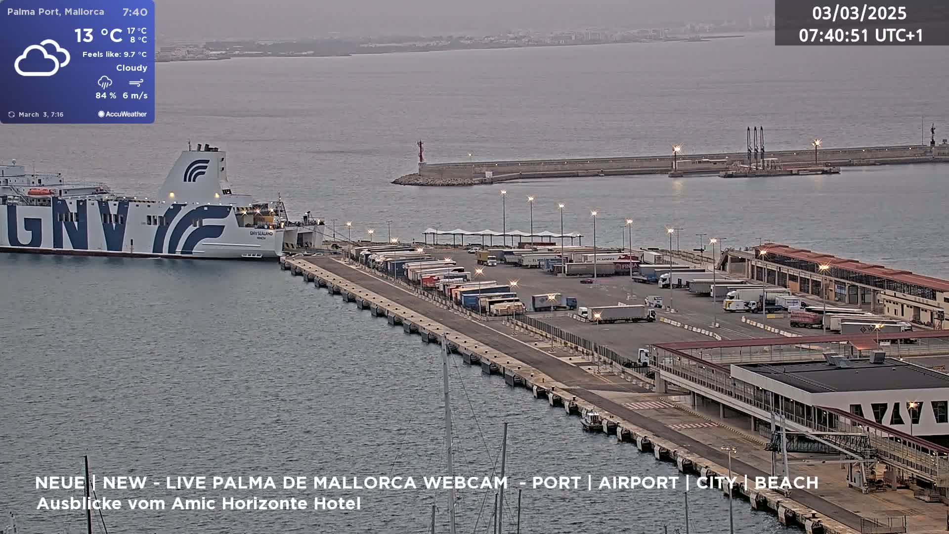 A ferry is docked at a port with numerous trucks parked on the pier under a cloudy sky.