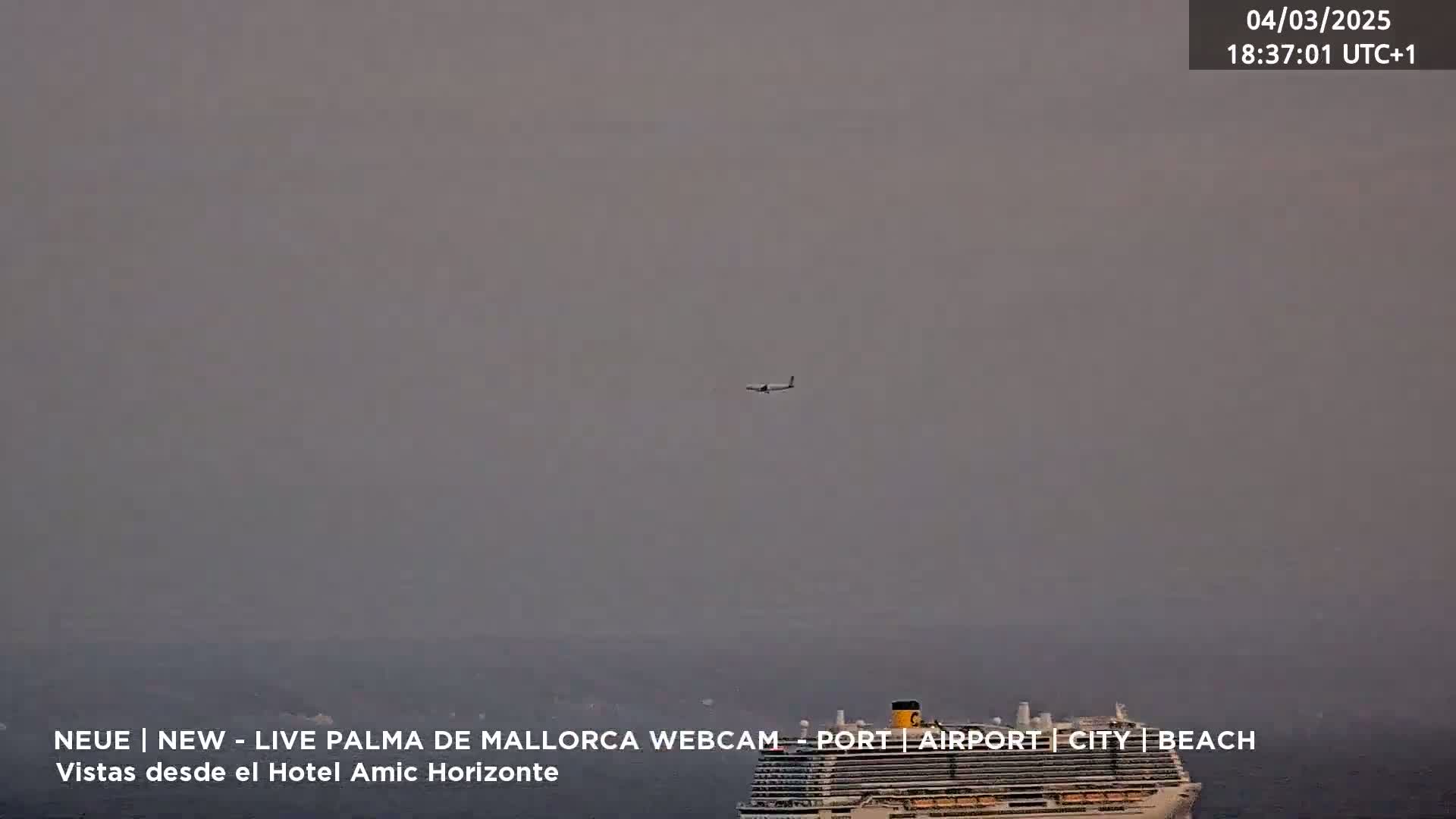 A hazy, overcast sky shows a cruise ship at sea with an airplane flying above it.