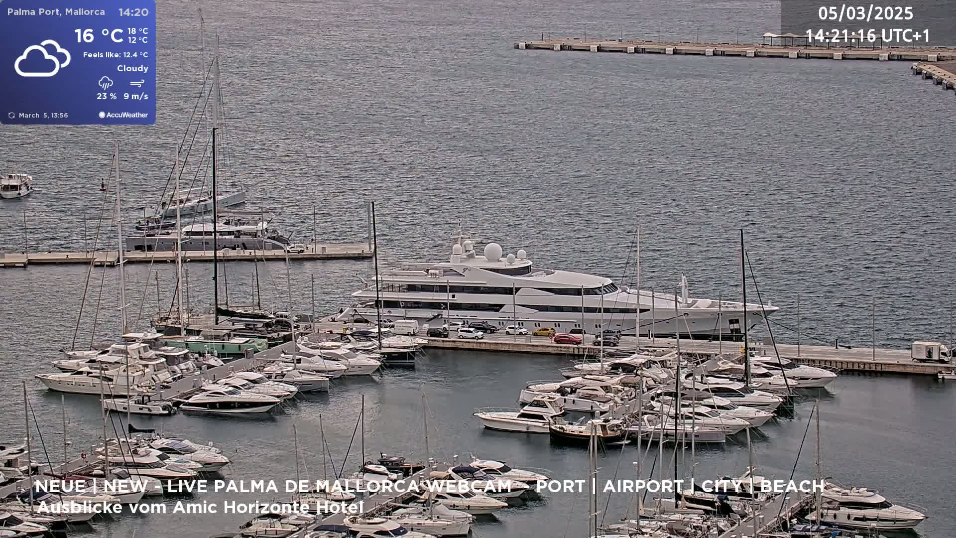 A large yacht is docked in a marina filled with numerous smaller boats under cloudy skies.