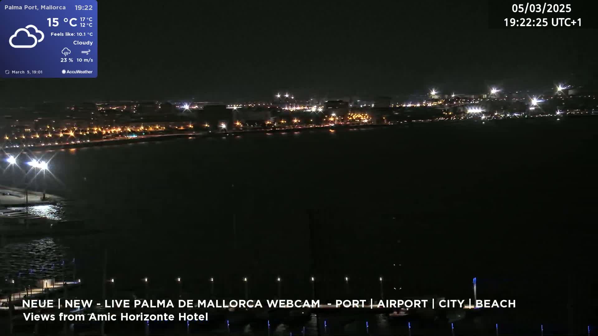 A nighttime, cloudy view of a city's illuminated waterfront across a dark body of water.