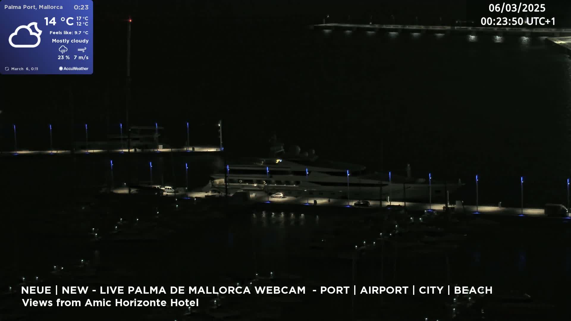 A mostly cloudy night scene shows a marina with a large yacht and smaller boats docked, illuminated by lights.