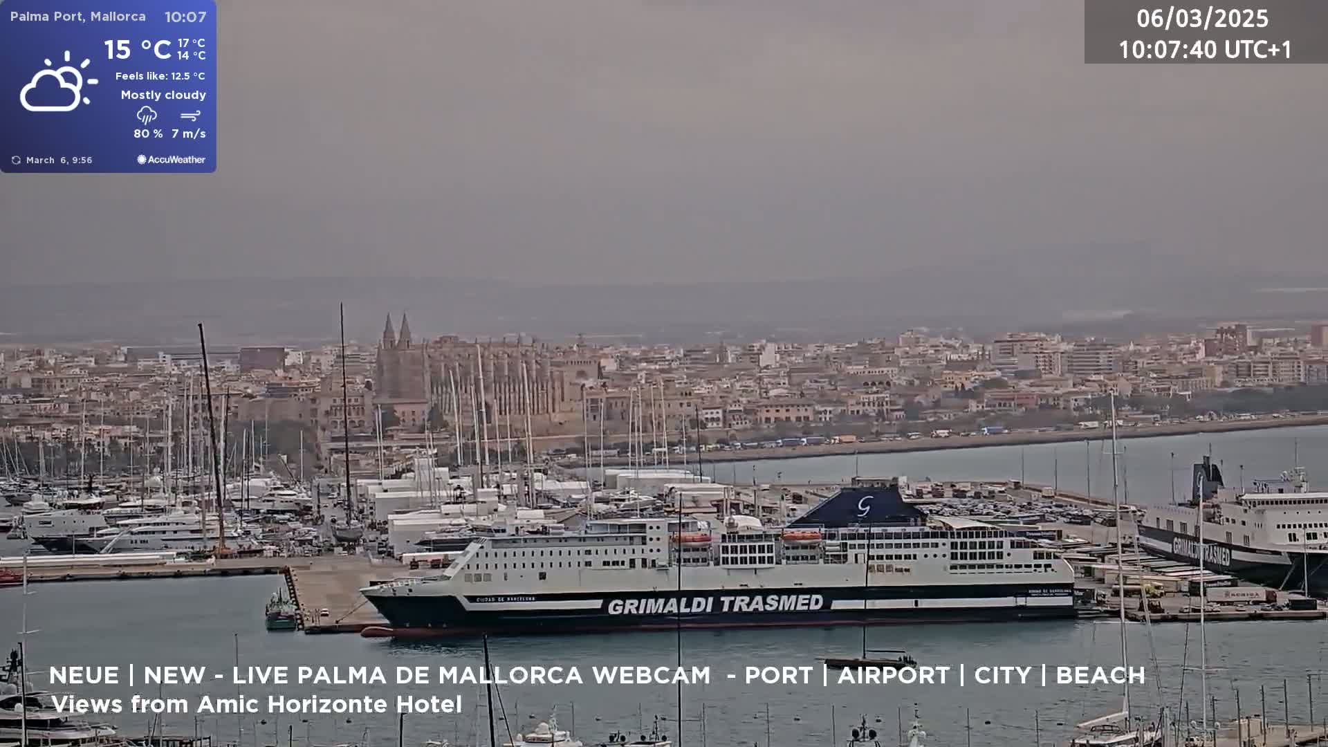 A mostly cloudy harbor scene shows a large ferry docked among many smaller boats, with a city and a cathedral visible in the background.