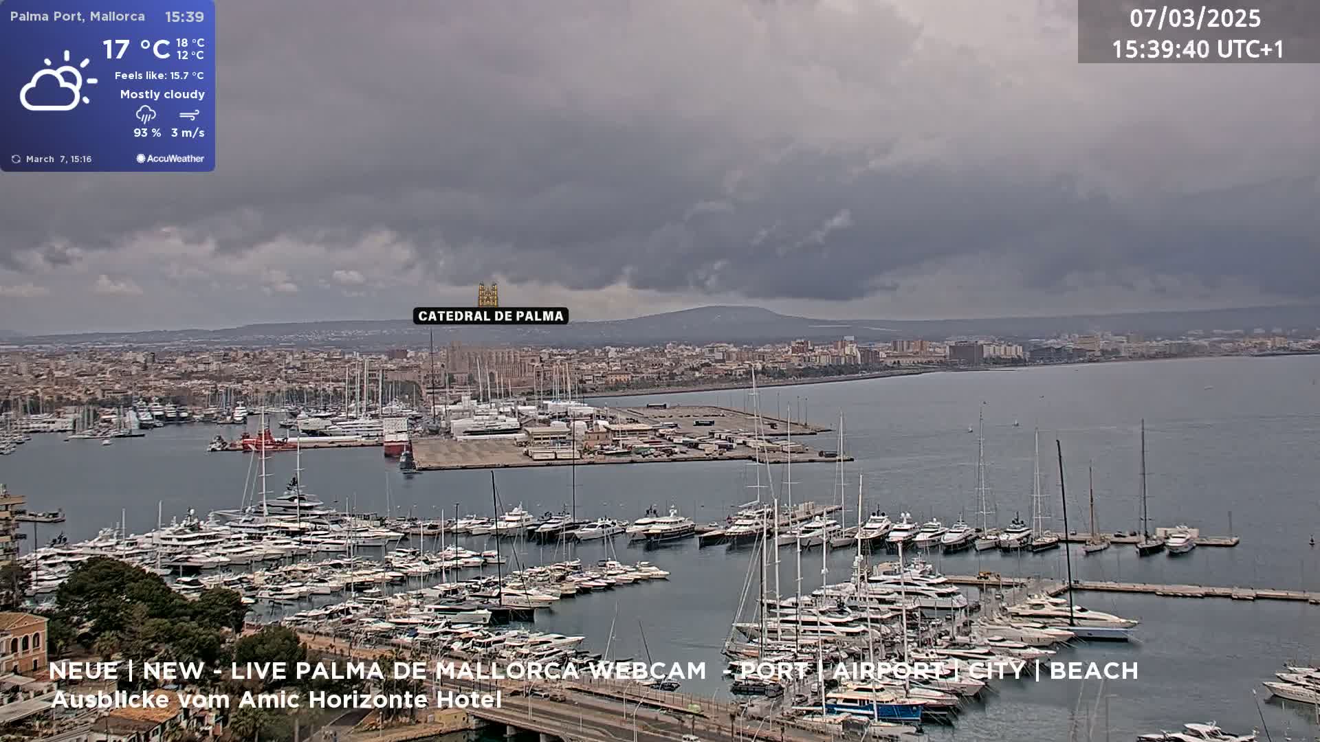 A mostly cloudy harbor filled with numerous yachts and boats, overlooked by a city and a cathedral under a gray sky.