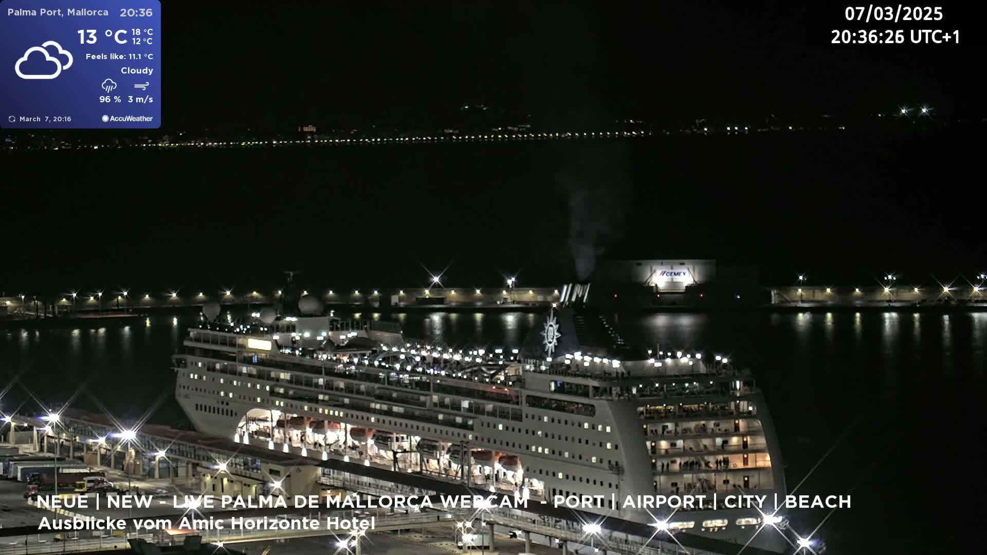 A large cruise ship is docked at a port at night under cloudy skies.