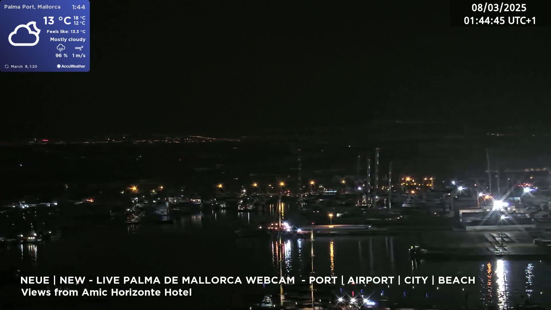 A nighttime view of a harbor with boats and city lights under a mostly cloudy sky.