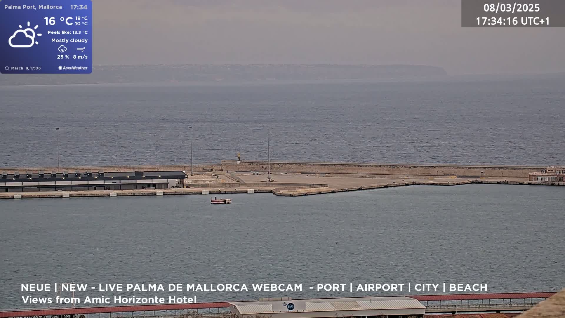 A mostly cloudy, breezy day overlooks a harbor with a small boat and a large building along the water's edge.