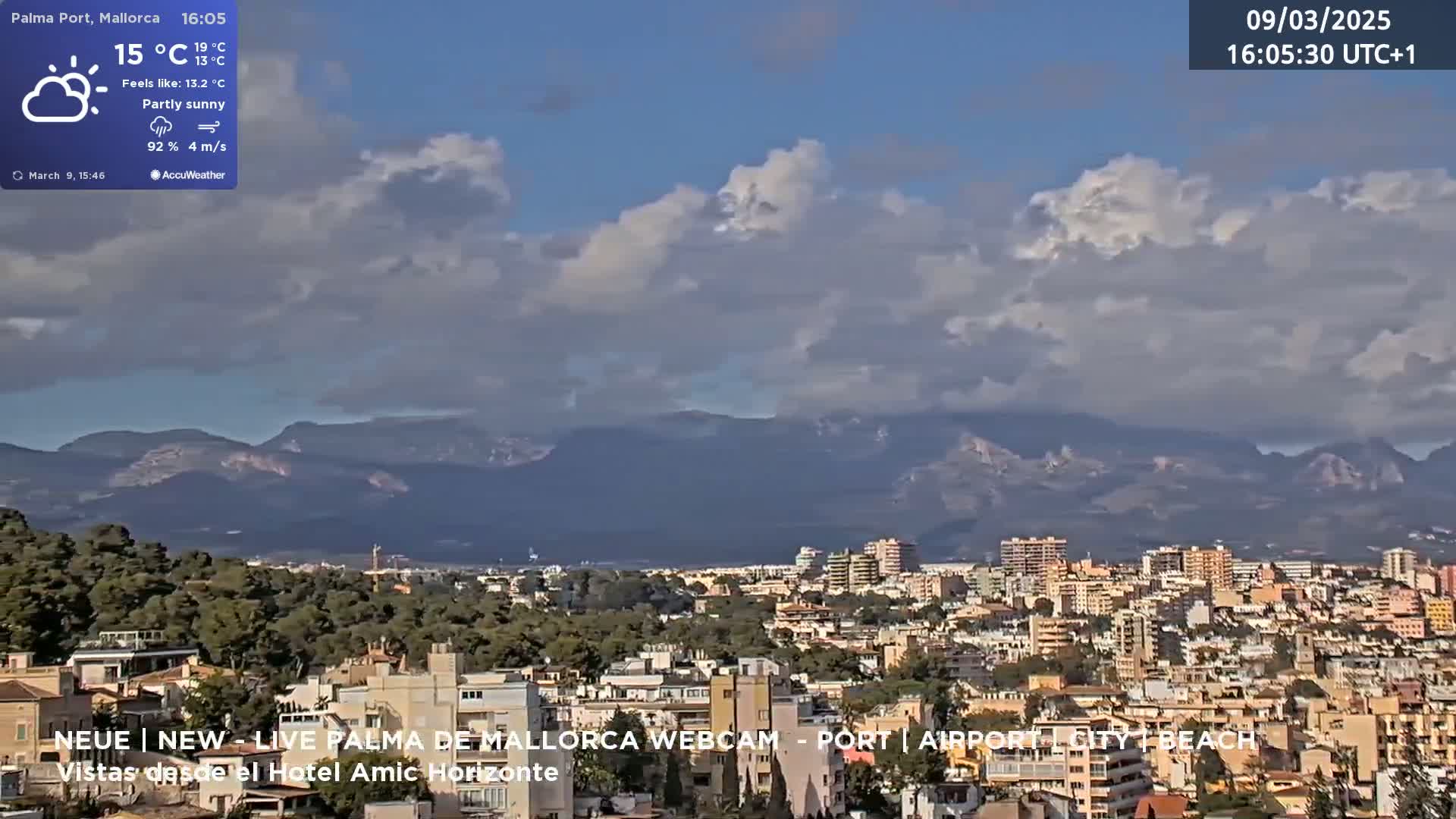 A partly sunny cityscape with mountains in the background is viewed from an elevated position.