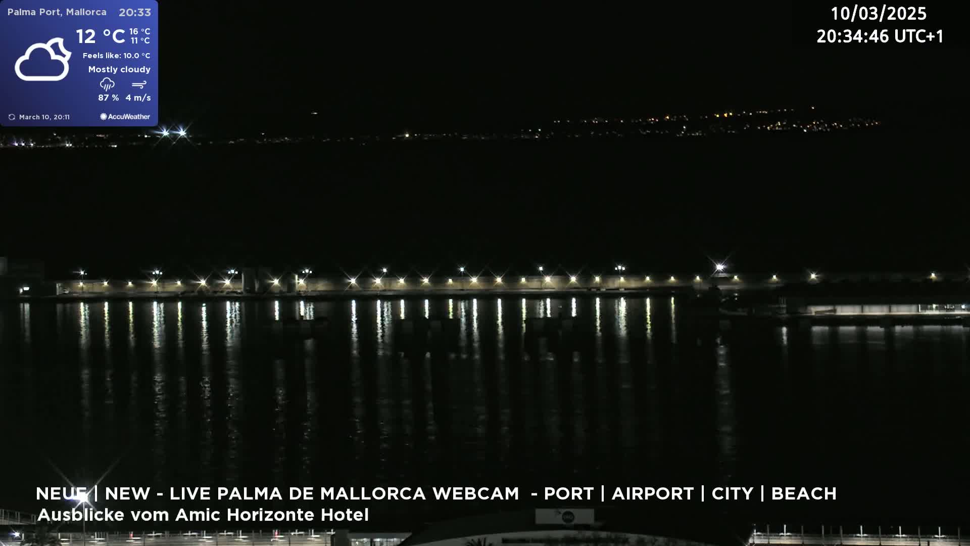A nighttime view of a calm body of water reflecting the lights of a waterfront structure under a mostly cloudy sky.
