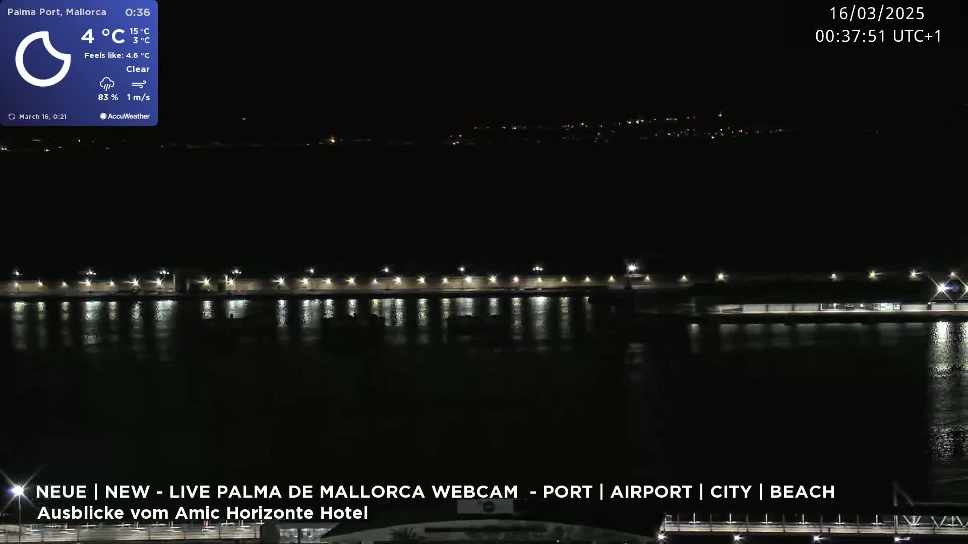 A nighttime view of a calm body of water reflecting the lights of a waterfront structure under a clear sky.