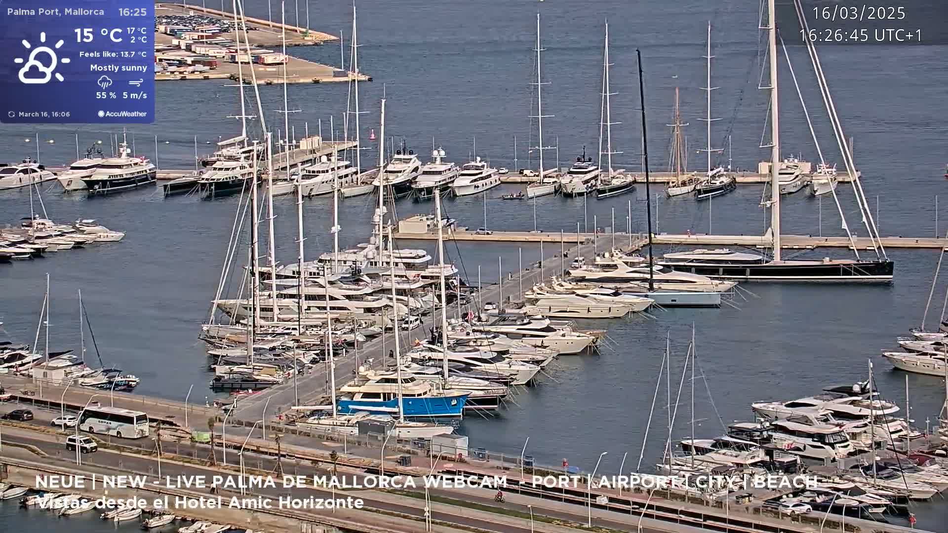 A mostly sunny marina filled with numerous yachts and sailboats is viewed from above.