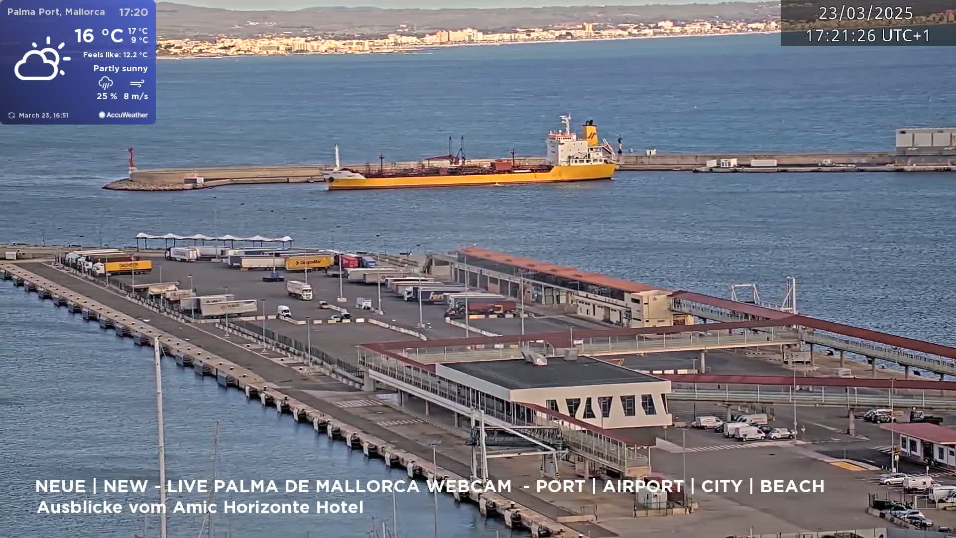 A partly sunny harbor scene shows a yellow tanker ship at a dock with numerous trucks parked in a large lot, all under a partly sunny sky.