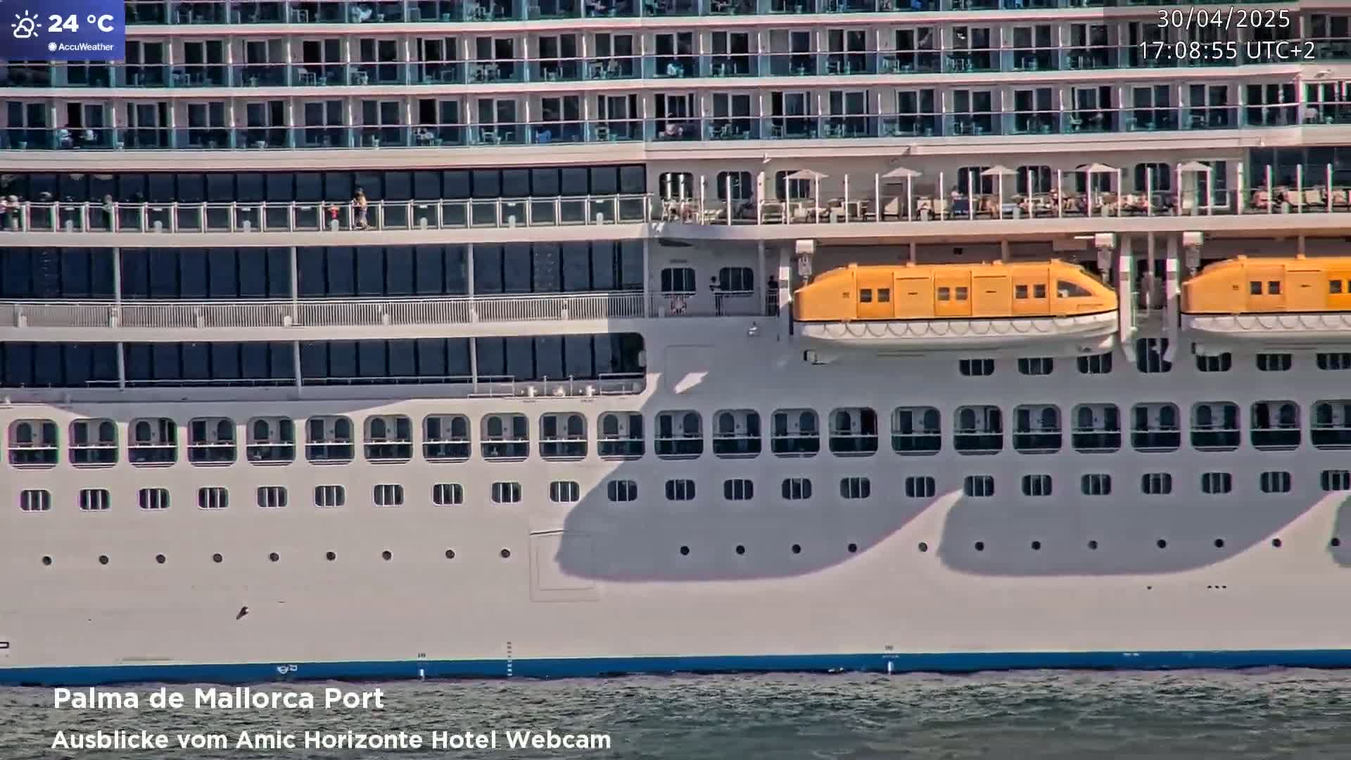 A large cruise ship is docked in calm water on a sunny day.