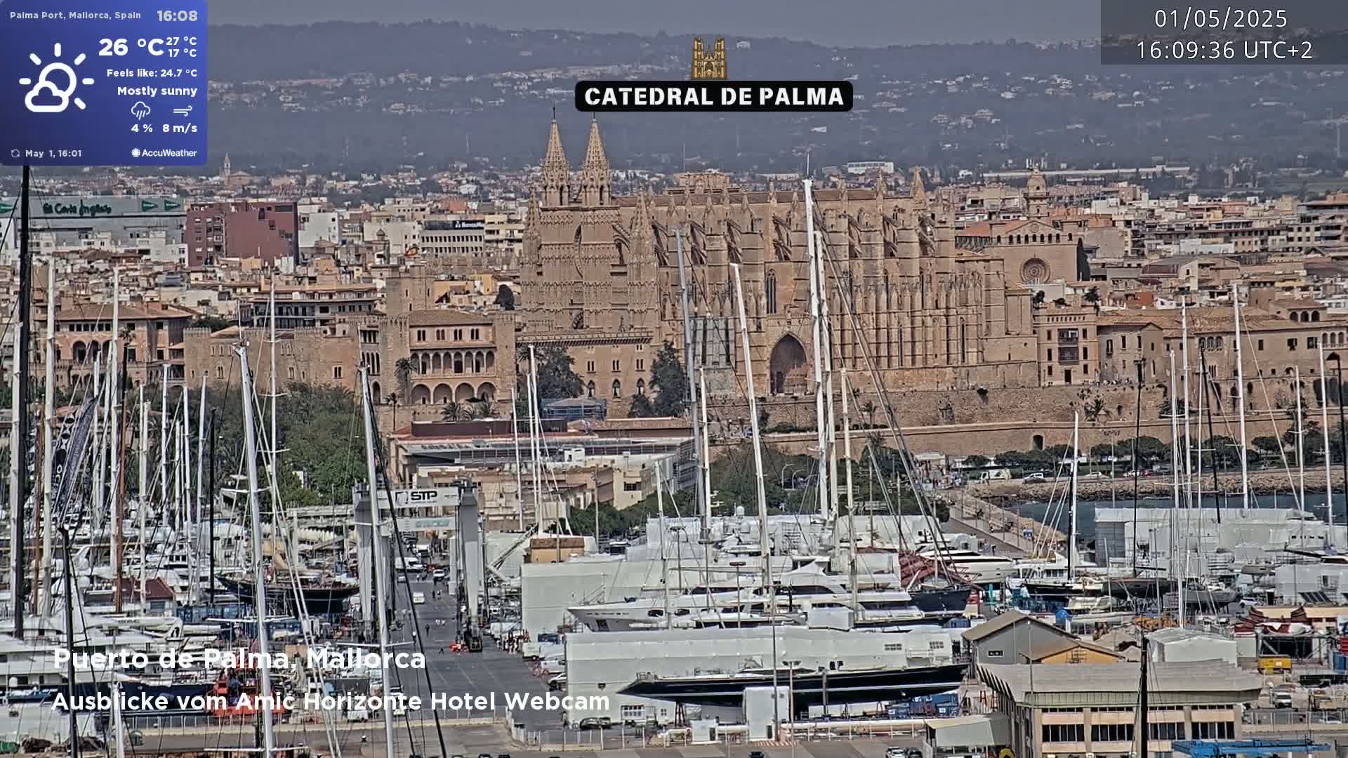 A mostly sunny view of Palma de Mallorca's harbor, filled with sailboats and yachts, with the Catedral de Palma prominently featured in the background.