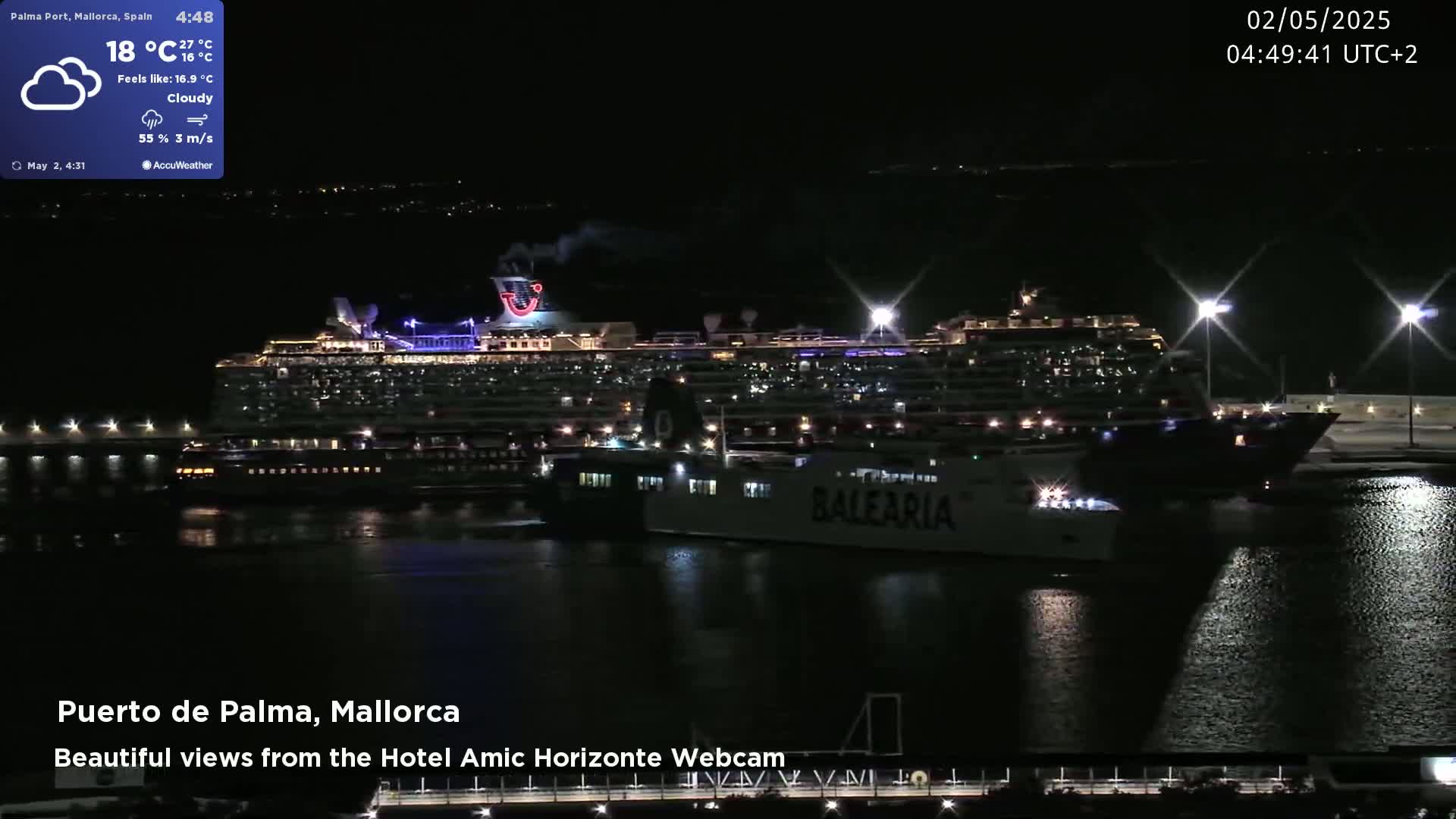 A large cruise ship and a smaller ferry are docked at a harbor at night under cloudy skies.