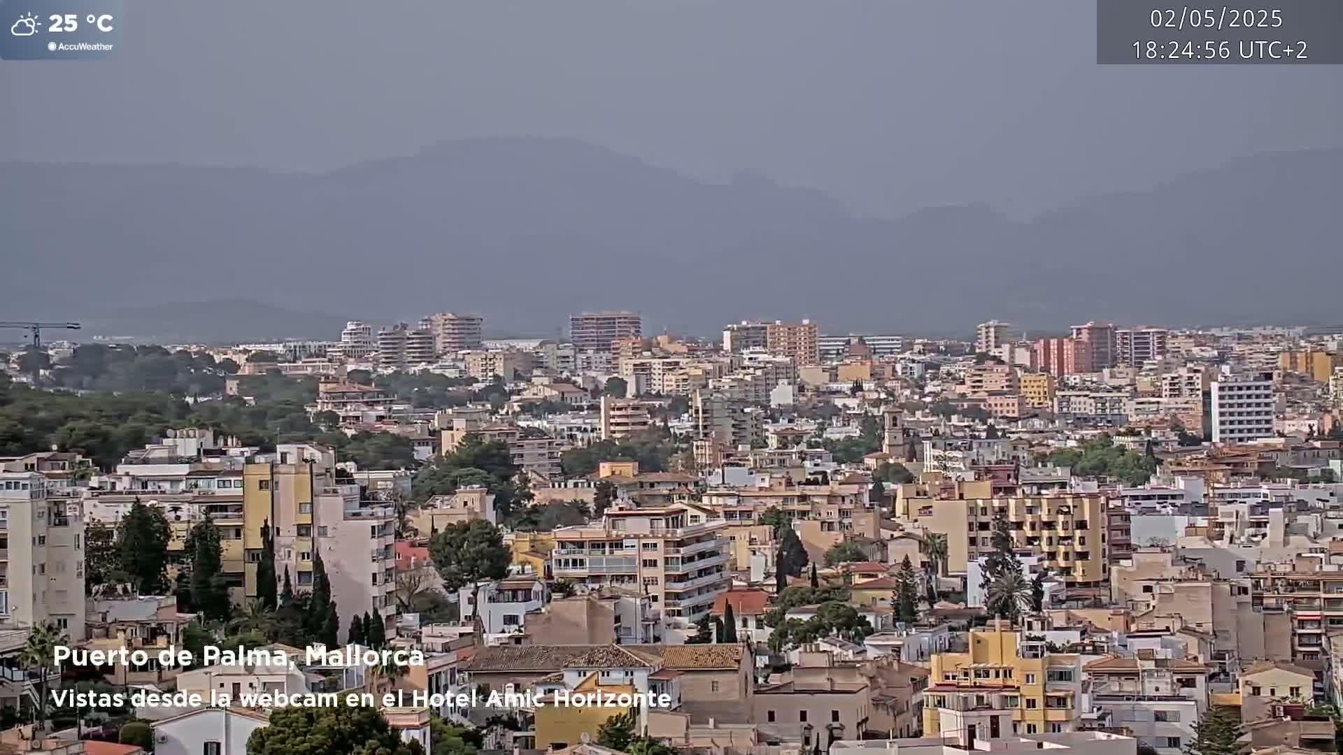 A hazy, 25°C cityscape of numerous buildings extends to distant mountains under a cloudy sky.