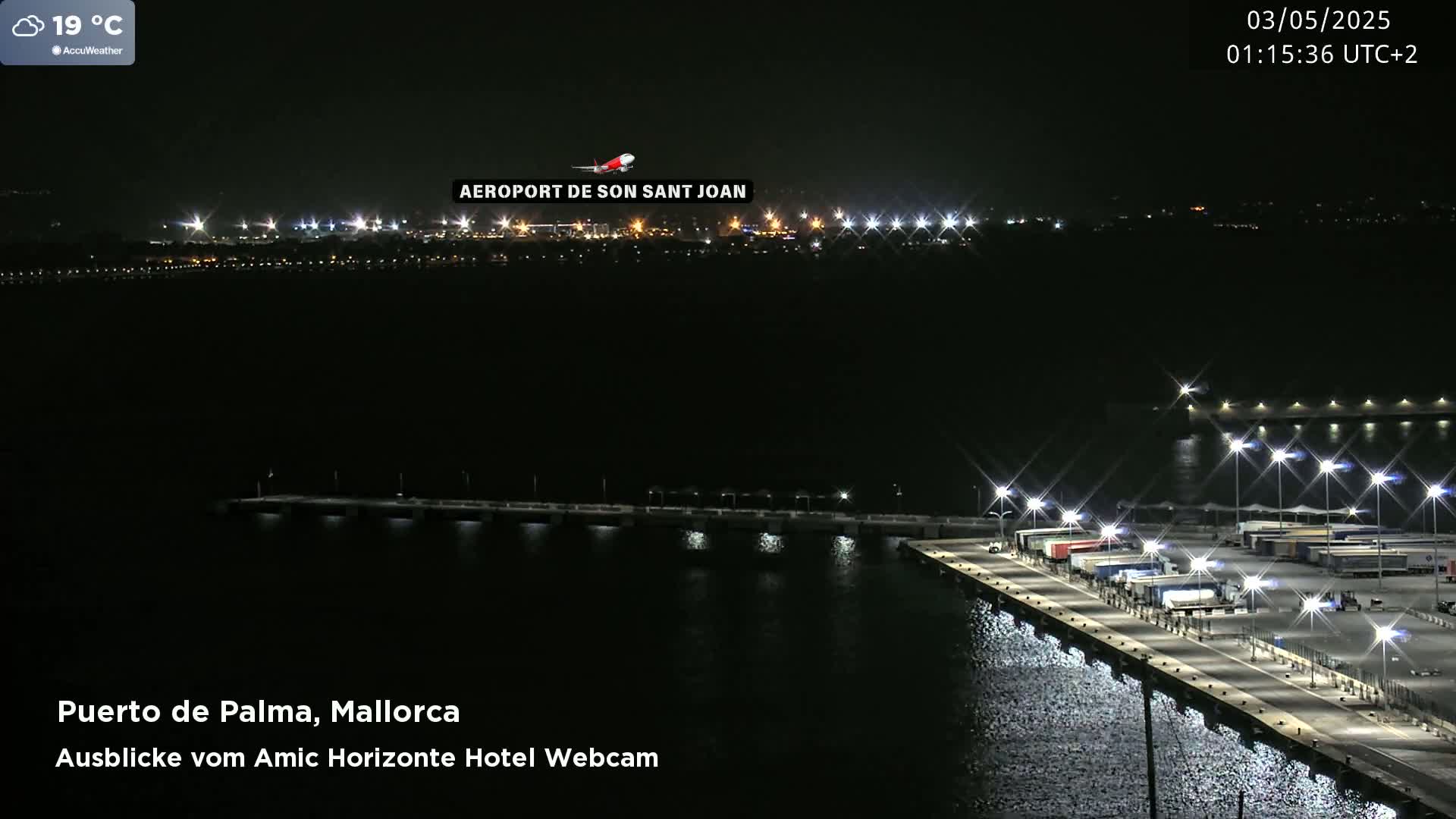 A nighttime view of a brightly lit port with a plane flying over a distant airport.