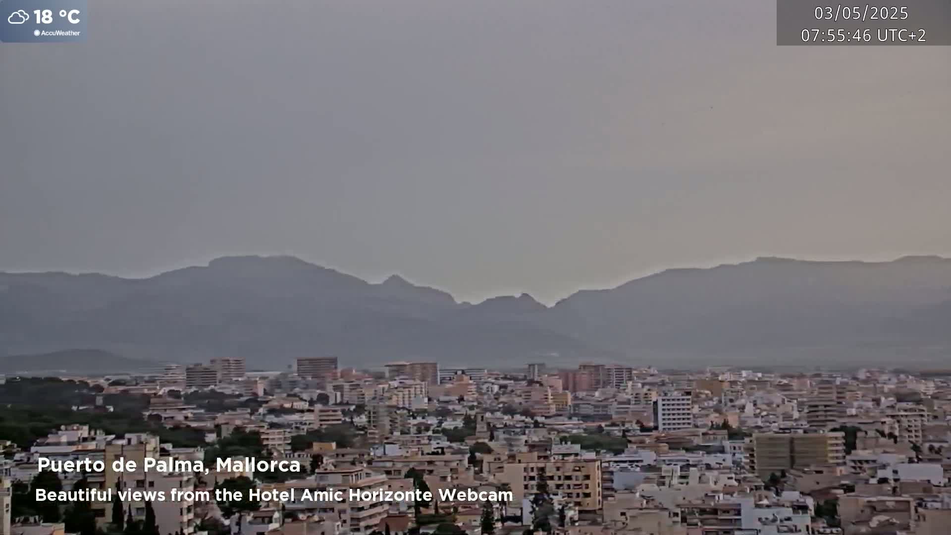 A hazy, overcast view shows a city sprawling beneath a mountain range in the distance.