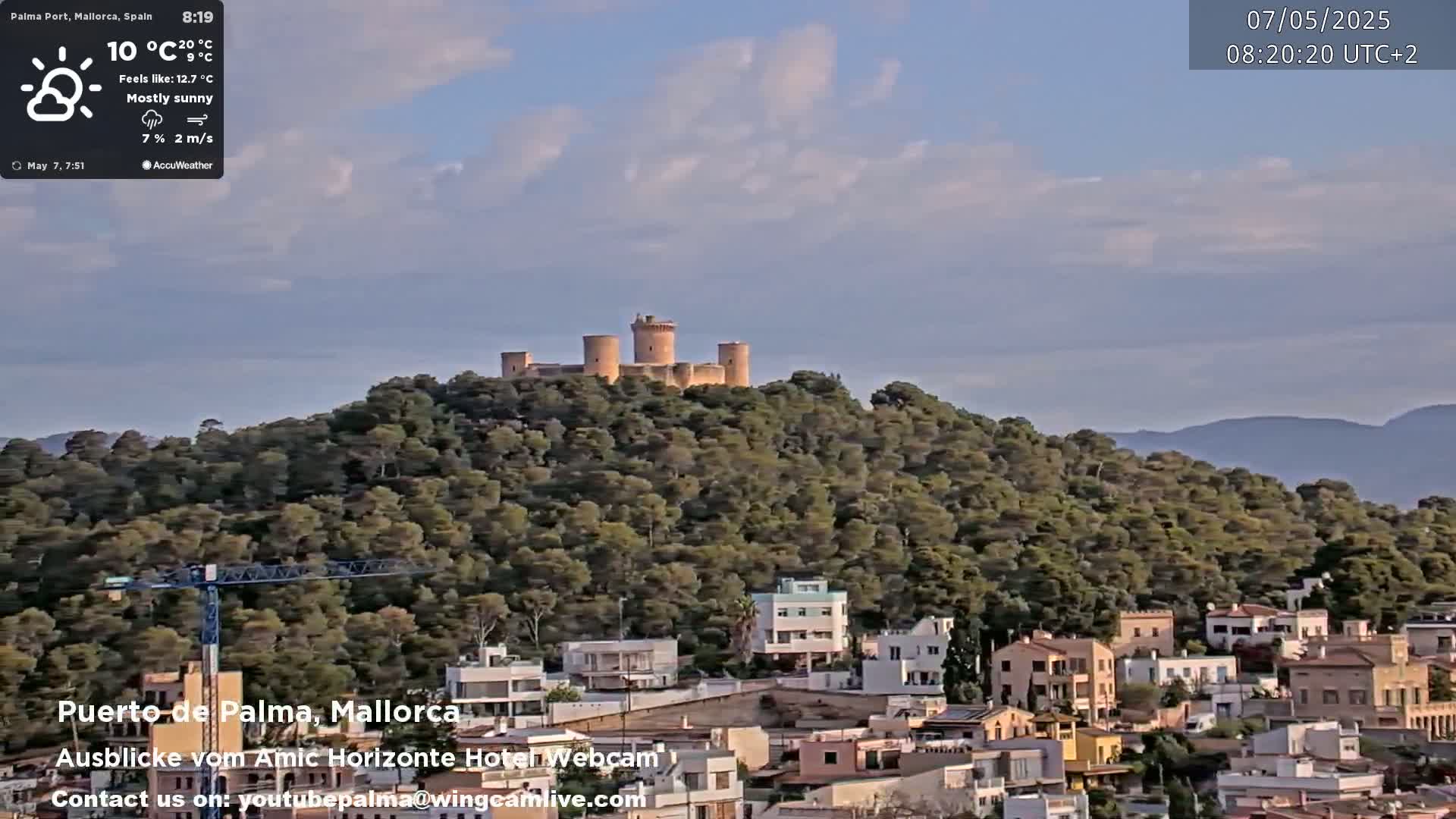 A mostly sunny day reveals a hilltop castle overlooking a town with low-rise buildings and a construction crane.