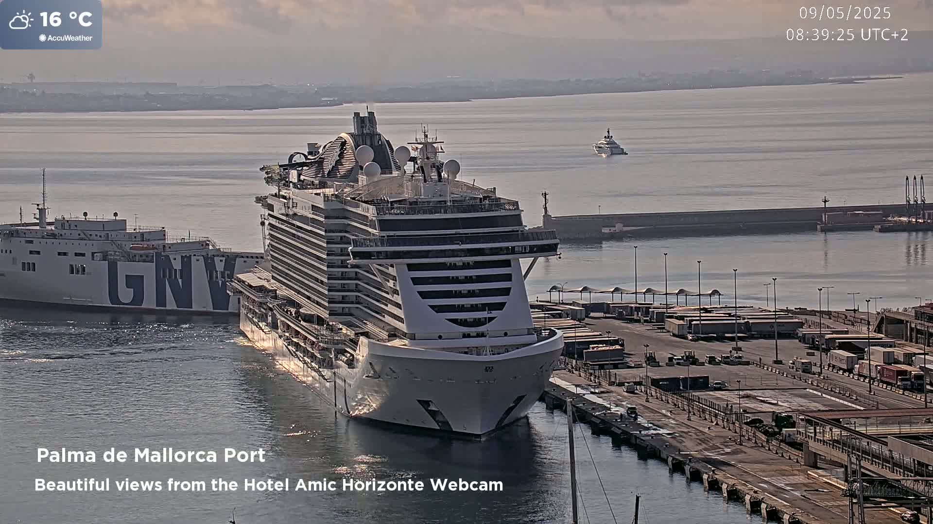 A large cruise ship and a cargo ship are docked at a port on a partly cloudy day with a temperature of 16 degrees Celsius.