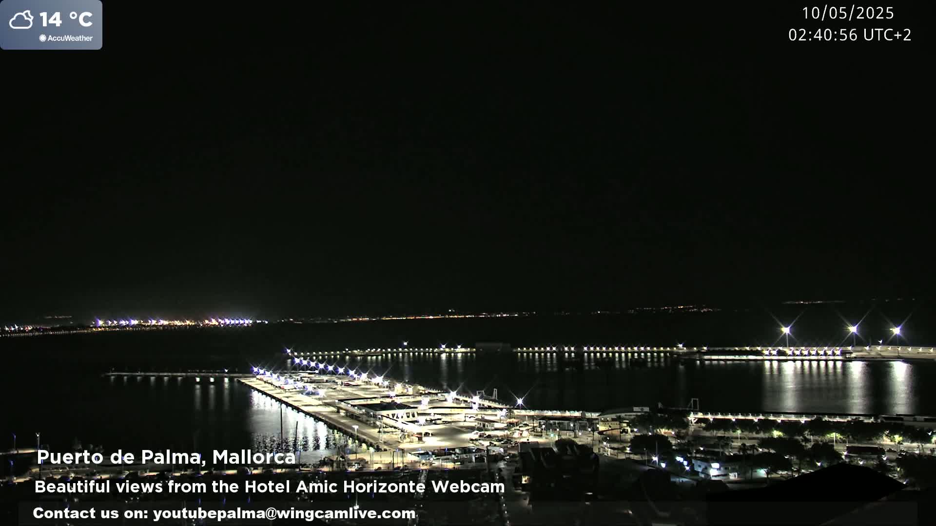 A nighttime, slightly cloudy view of a harbor illuminated by lights, with a temperature of 14 degrees Celsius.