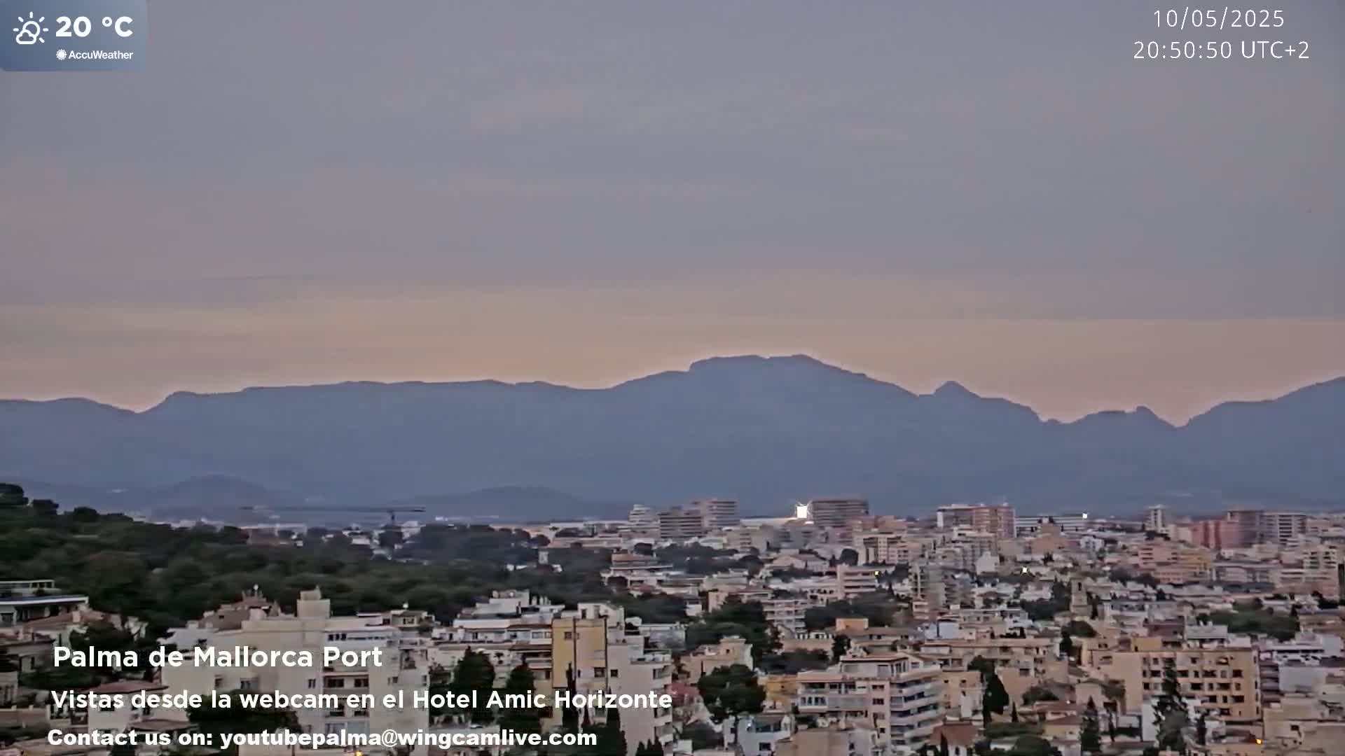 A city skyline with a mountain range in the background under a twilight sky.