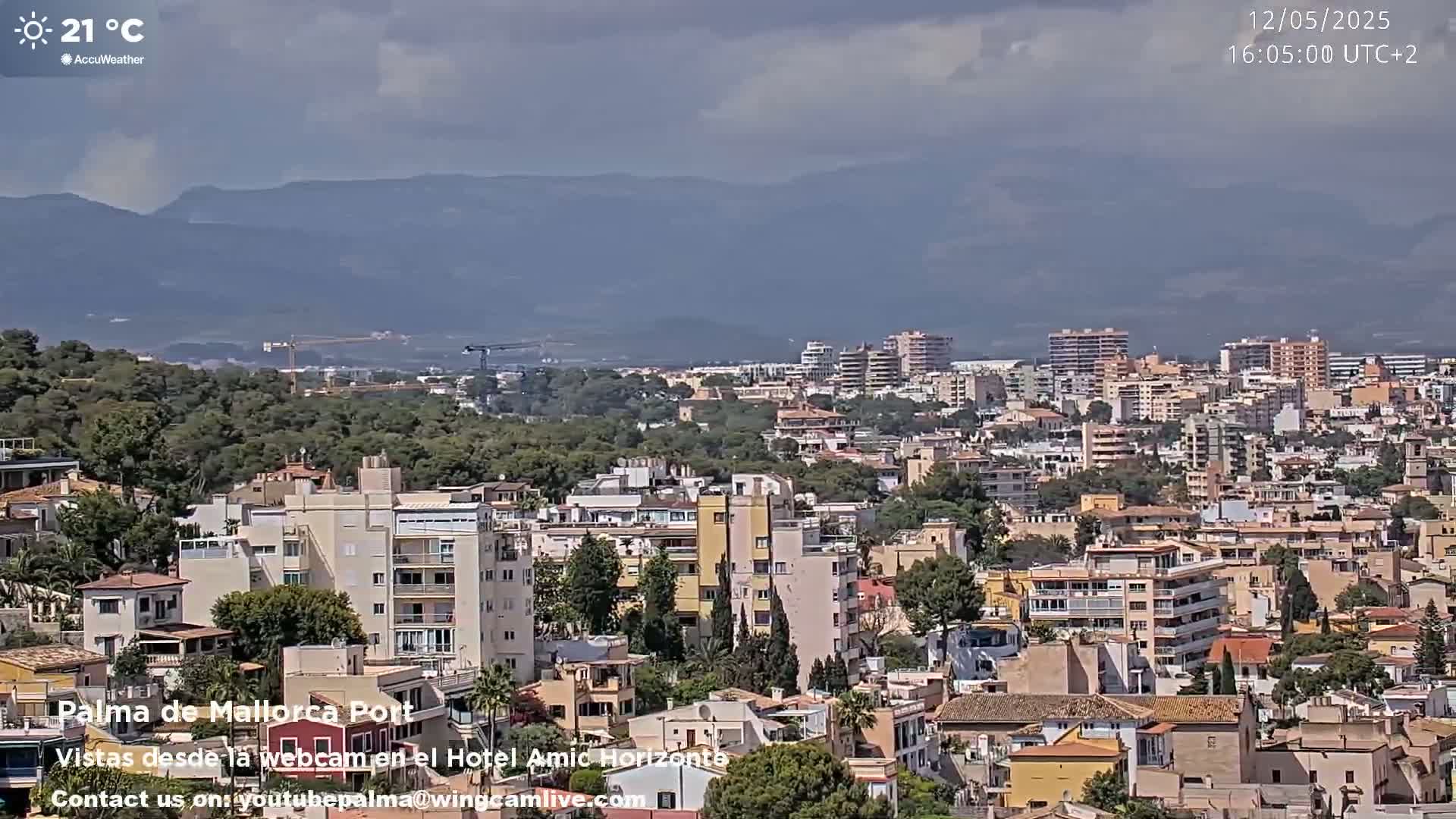 A sprawling city with many multi-story buildings nestles against a backdrop of distant mountains under a partly cloudy sky.