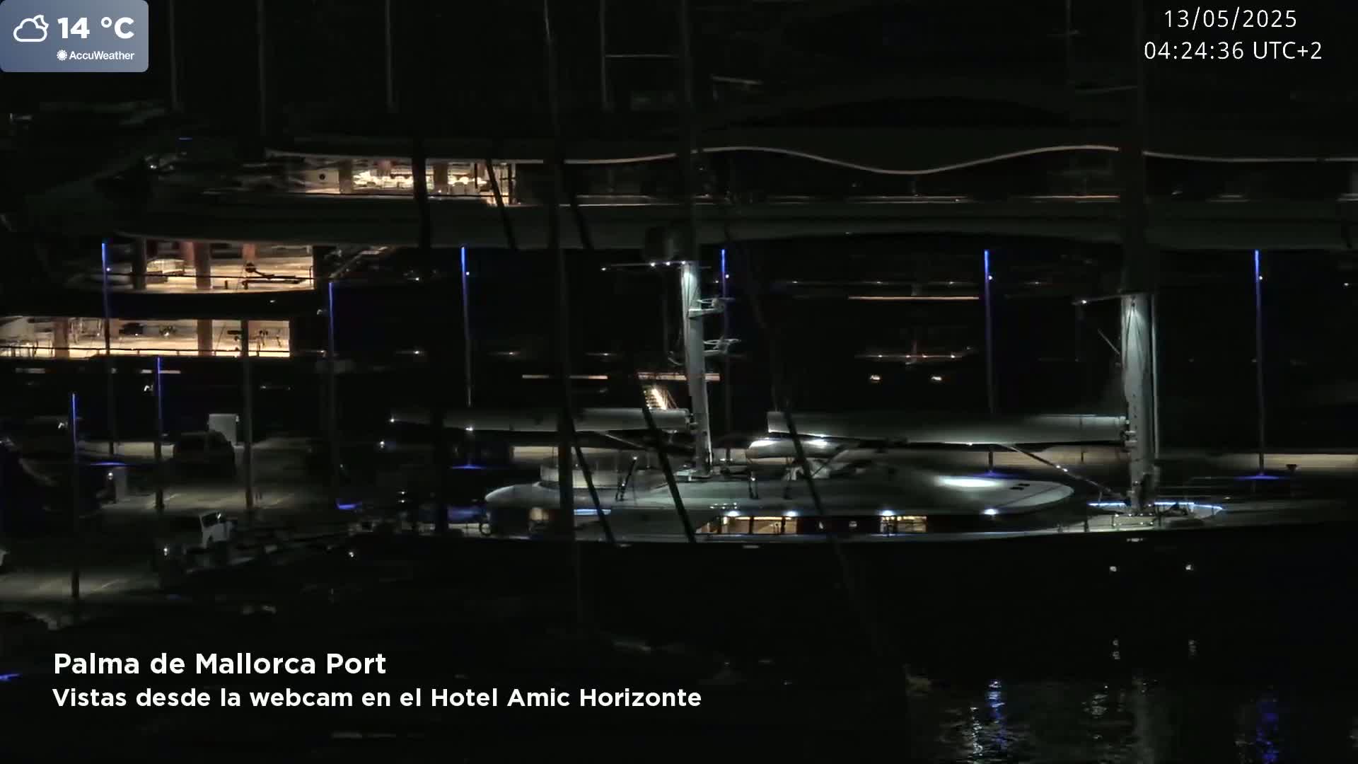 A large yacht is docked at a marina at night under a partly cloudy sky with a temperature of 14 degrees Celsius.