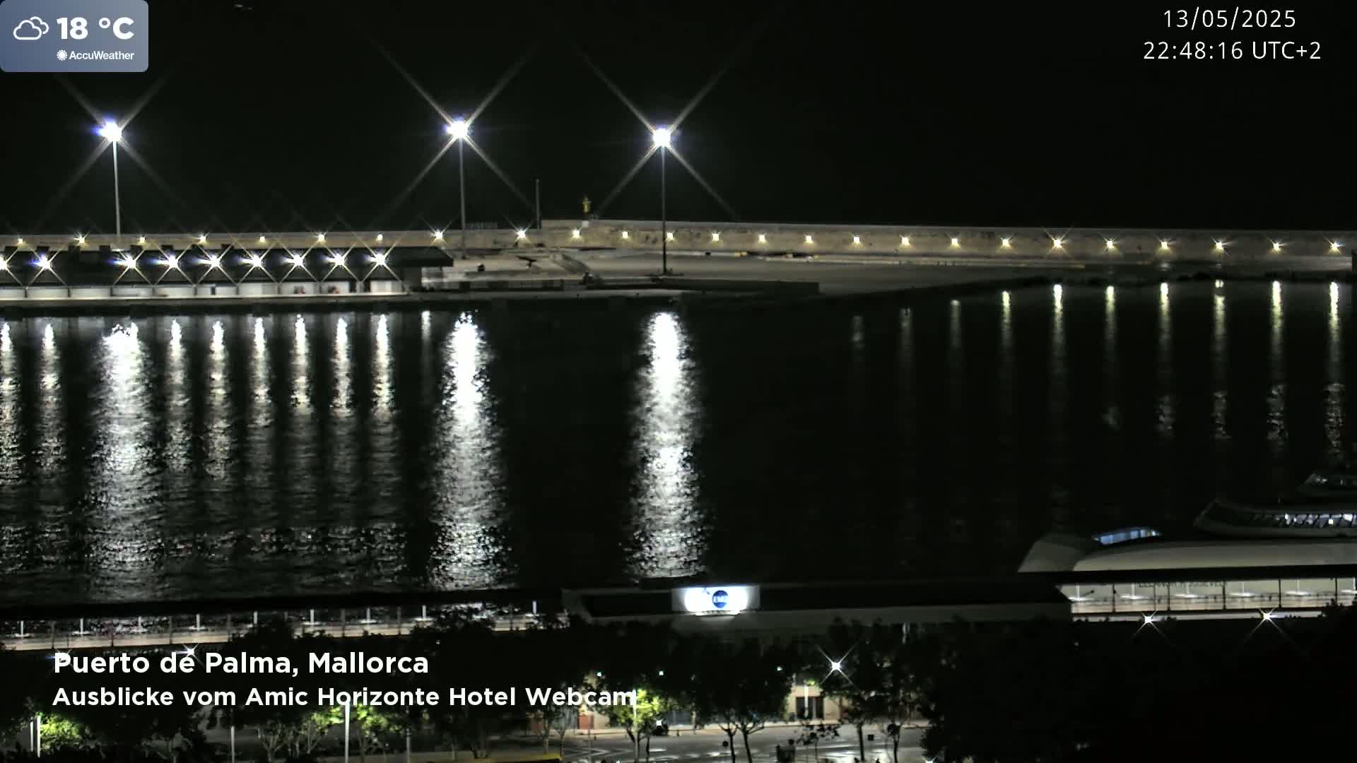 A nighttime view of a harbor, illuminated by bright lights reflecting on calm water, with a boat visible in the lower right.