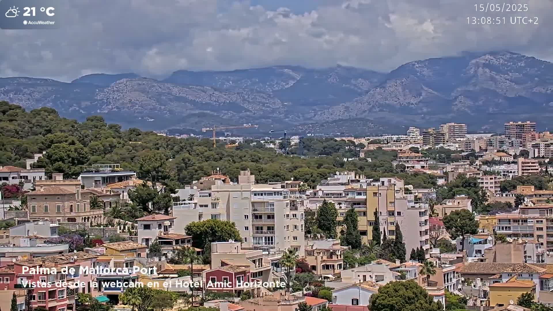A partly cloudy day reveals a cityscape nestled among green hills and mountains, with a temperature of 21 degrees Celsius.