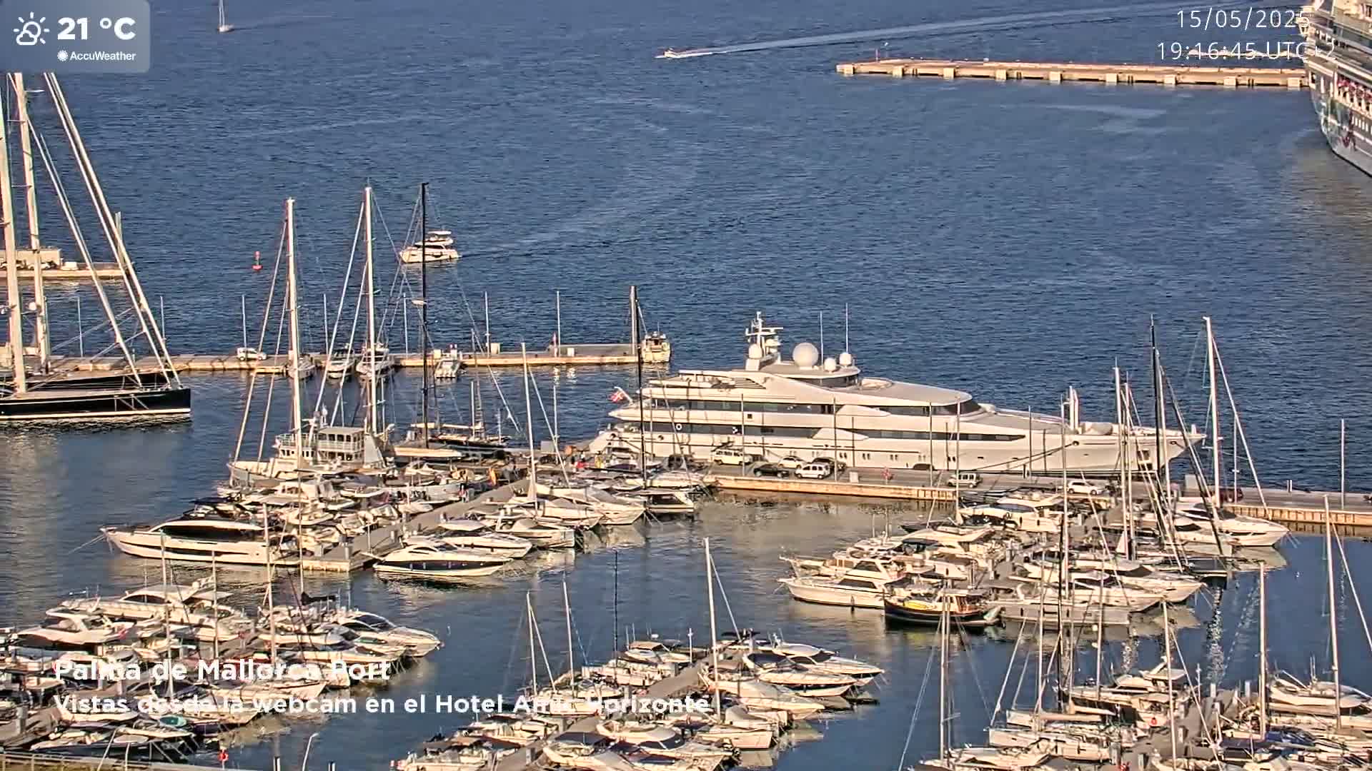 A marina filled with numerous yachts and sailboats on a calm, sunny day with a large luxury yacht prominently docked.