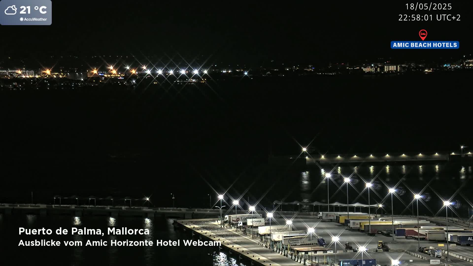 A nighttime long shot of a harbor with many illuminated trucks and buildings in the distance, under a clear sky.