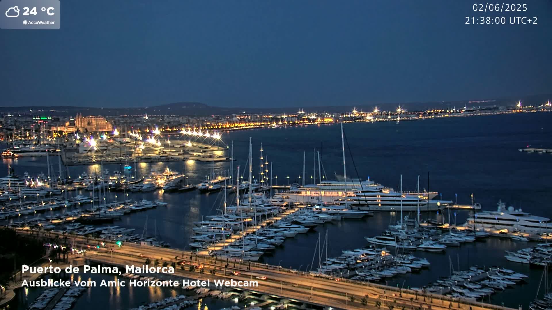 A nighttime harbor filled with numerous yachts and boats is illuminated under a partly cloudy sky.