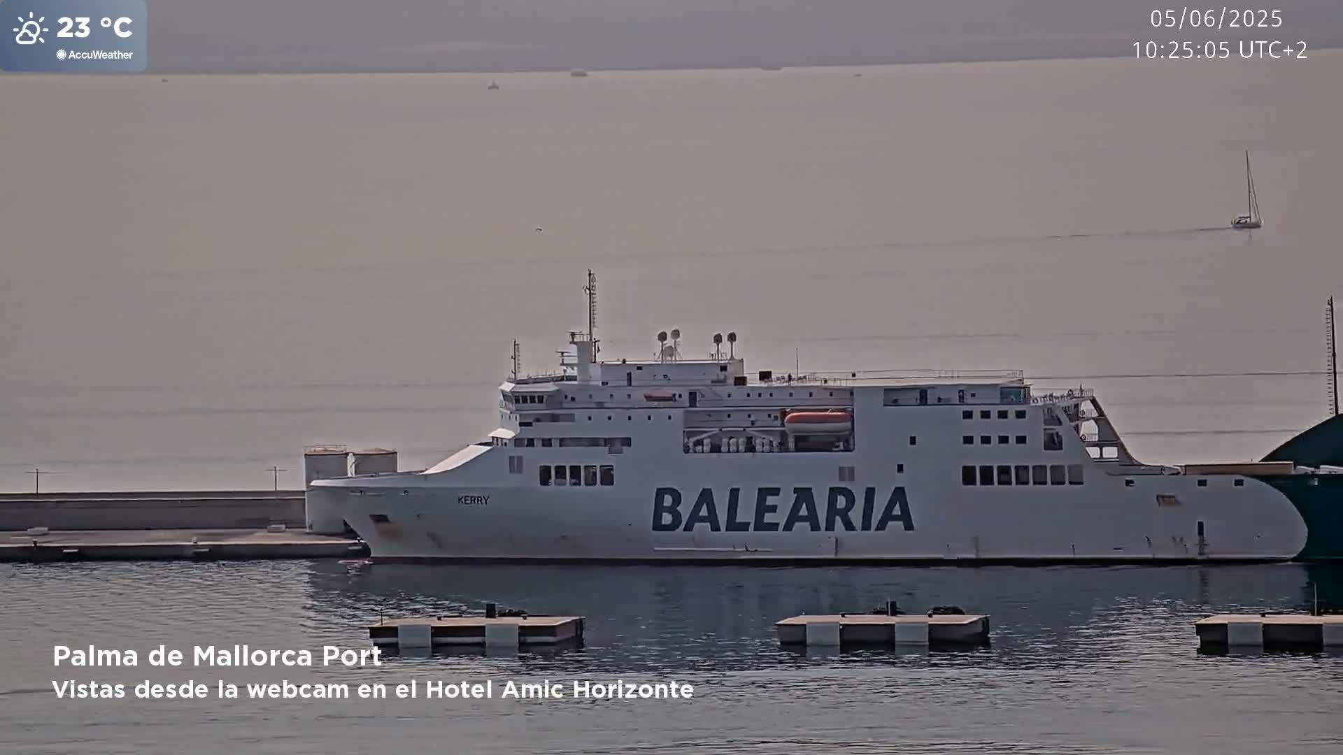A large white ferry named "BALEARIA" is docked at a port on a hazy, sunny day with a temperature of 23°C.