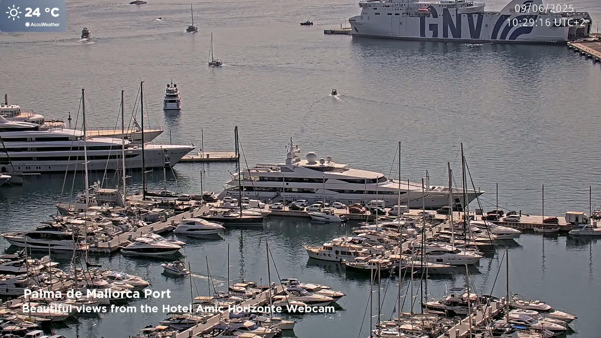 A marina filled with numerous yachts and boats on a sunny day, with a large ferry visible in the background.