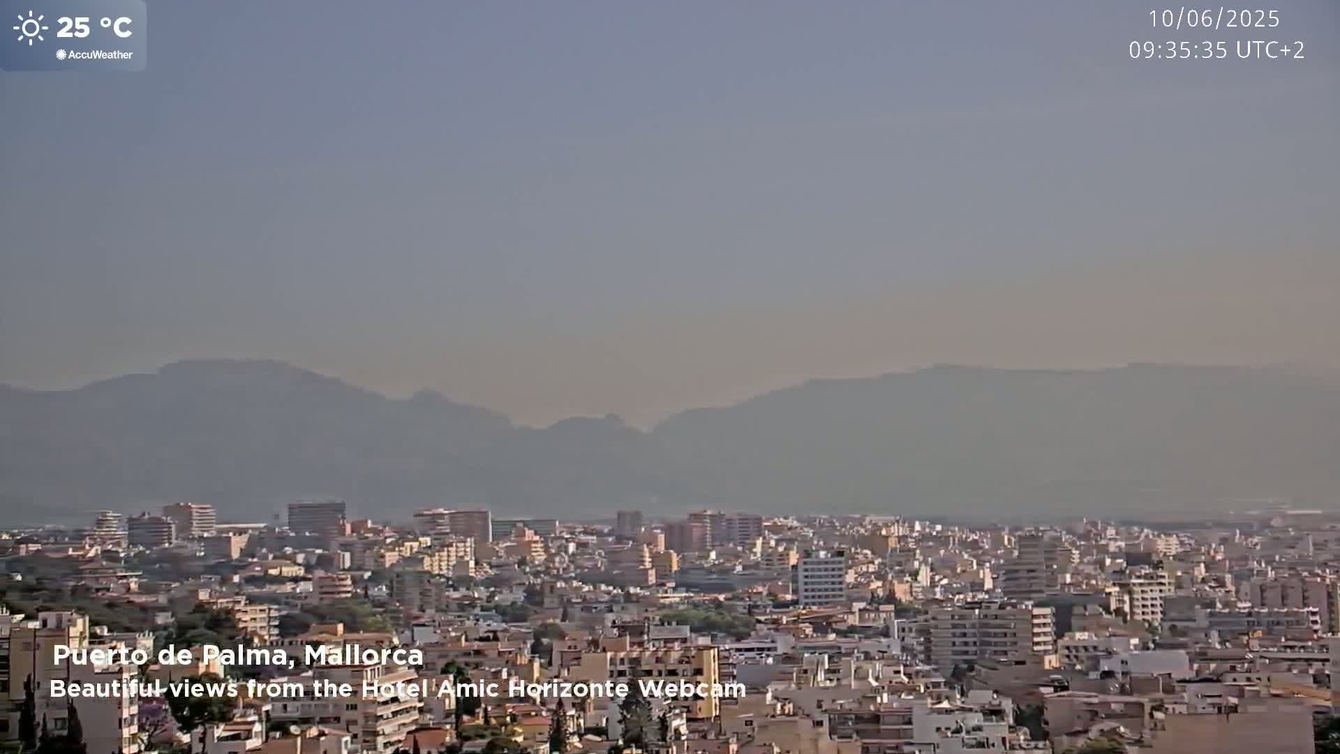 A hazy, sunny view of a city nestled at the foot of distant mountains, with a temperature of 25 degrees Celsius.
