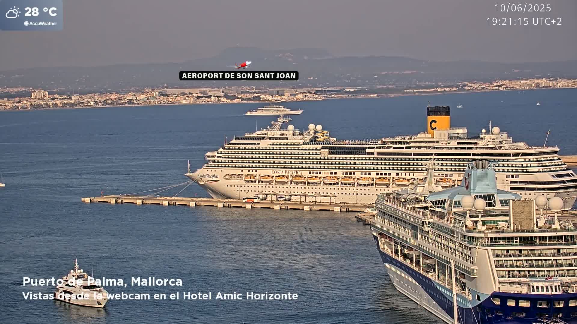 A hazy, sunny day shows two large cruise ships docked at a port, with a smaller yacht nearby, and another ship visible further out in the water.