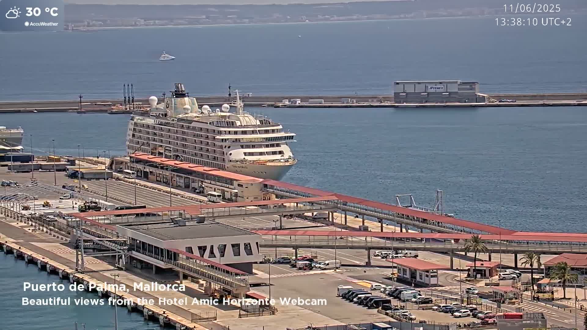 A large cruise ship is docked at a port on a sunny day with calm water and a temperature of 30 degrees Celsius.