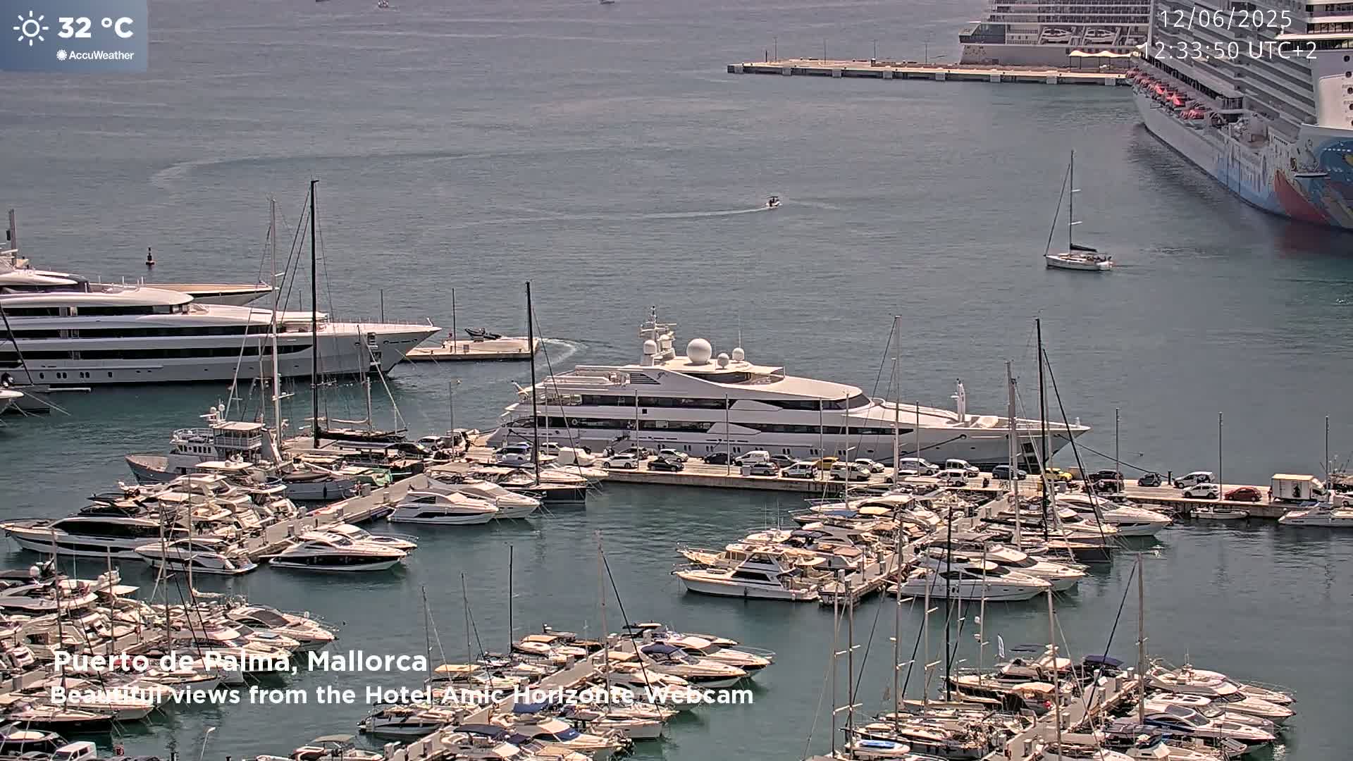 A marina filled with numerous yachts and boats on a sunny day with a temperature of 32 degrees Celsius, and a large cruise ship is visible in the background.