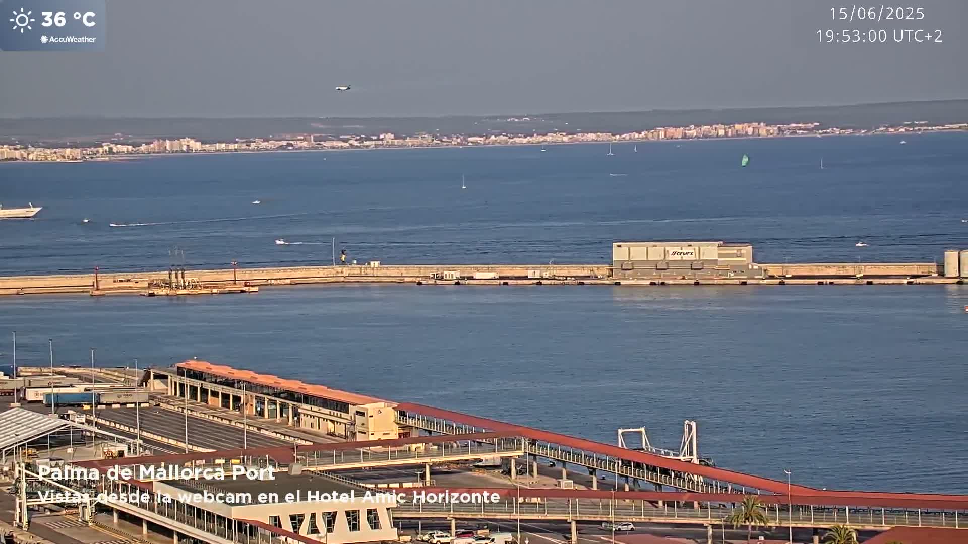 A harbor with a long pier and several boats, under a clear, sunny sky with a temperature of 36 degrees Celsius.
