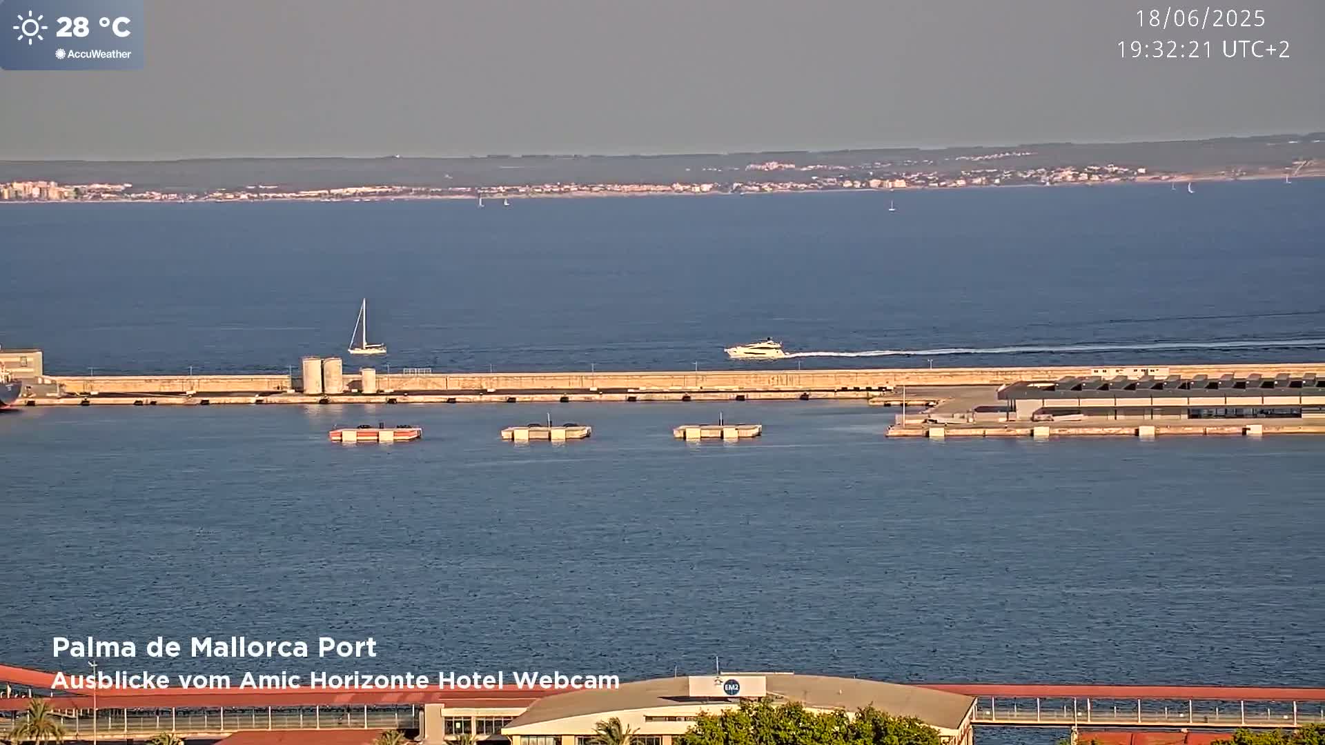 A harbor with several boats and a long dock, under a clear, sunny sky at 28°C.