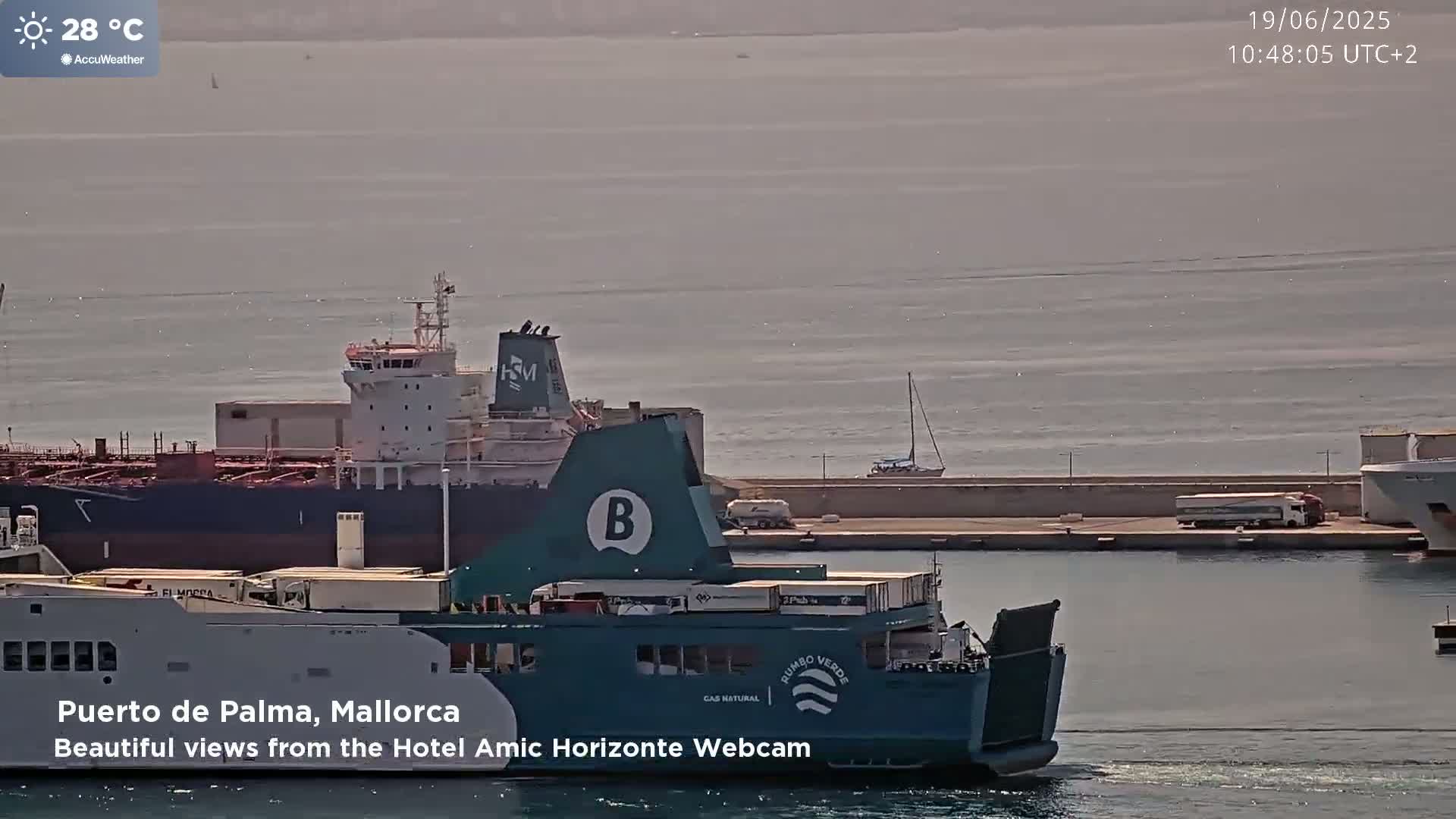 A large ferry is docked next to a tanker ship in calm waters under a sunny sky.